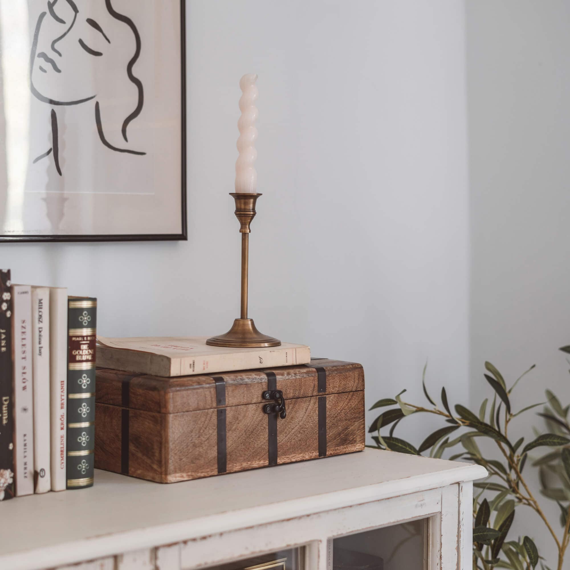 Boîte en bois marron avec bandes métalliques sur commode blanche avec livres et bougie