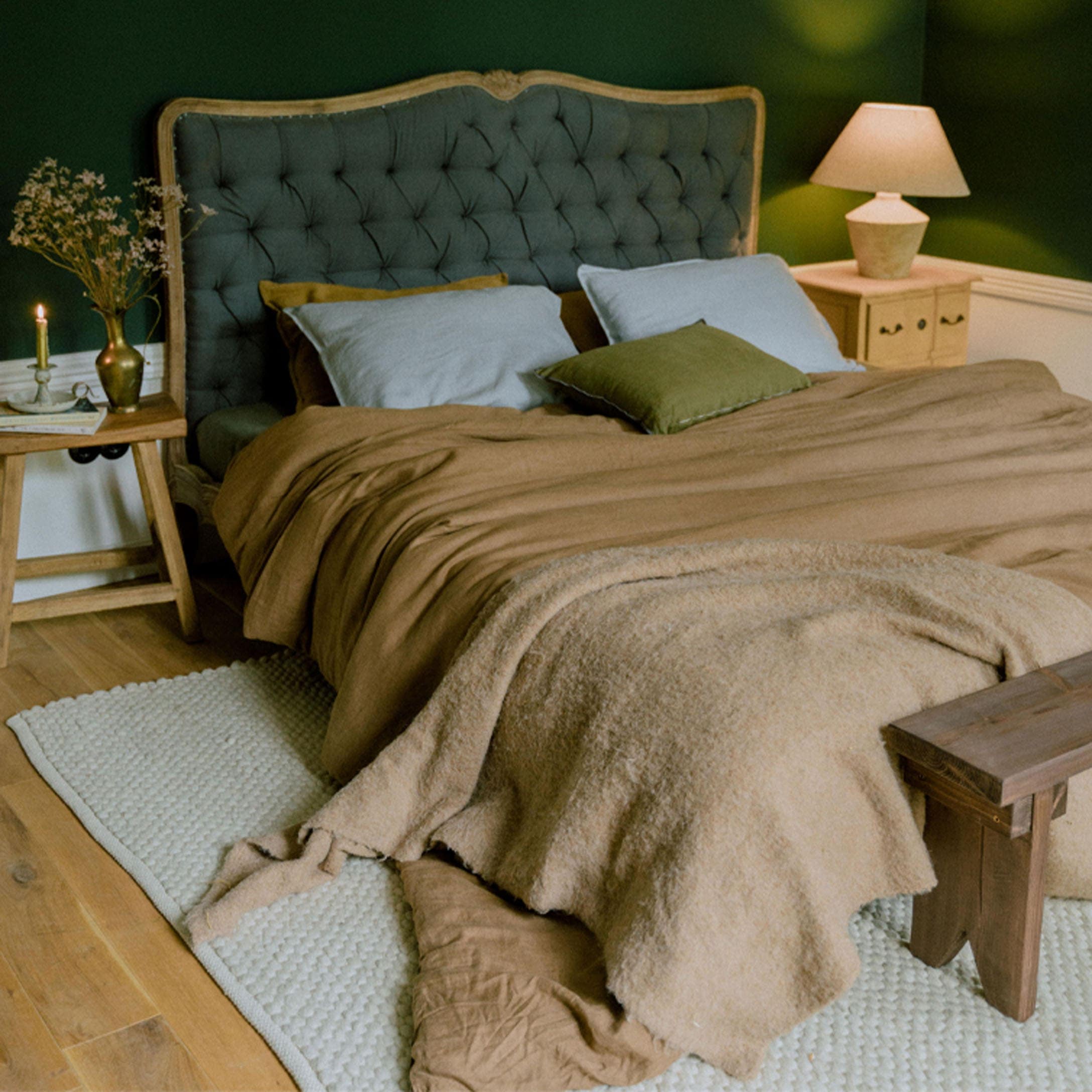 Lit confortable avec tête de lit capitonnée verte et linge de lit marron dans une chambre chaleureuse