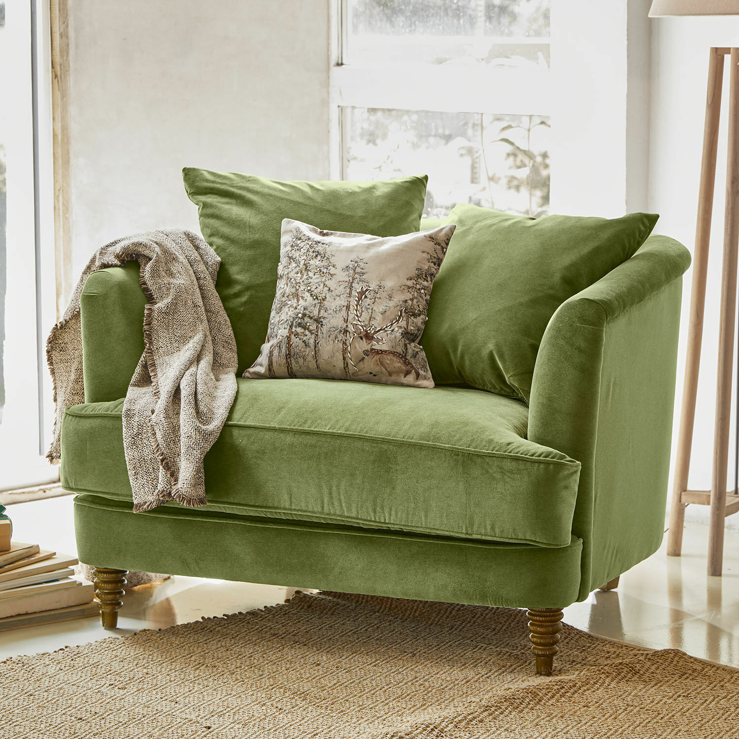 Fauteuil Etueffont Canapé vert en velours avec coussins et plaid beige sur tapis naturel dans une pièce lumineuse