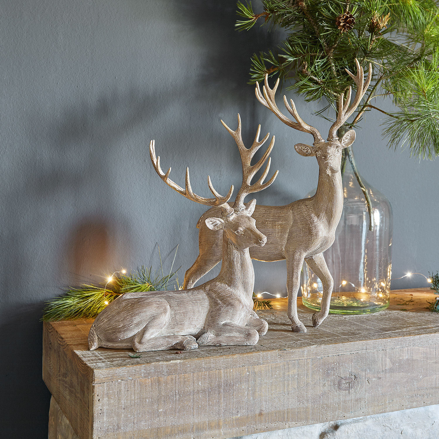 Lot de 2 cerfs Barima Deux figurines de cerfs en bois couleur naturelle sur une table en bois avec des branches vertes décoratives