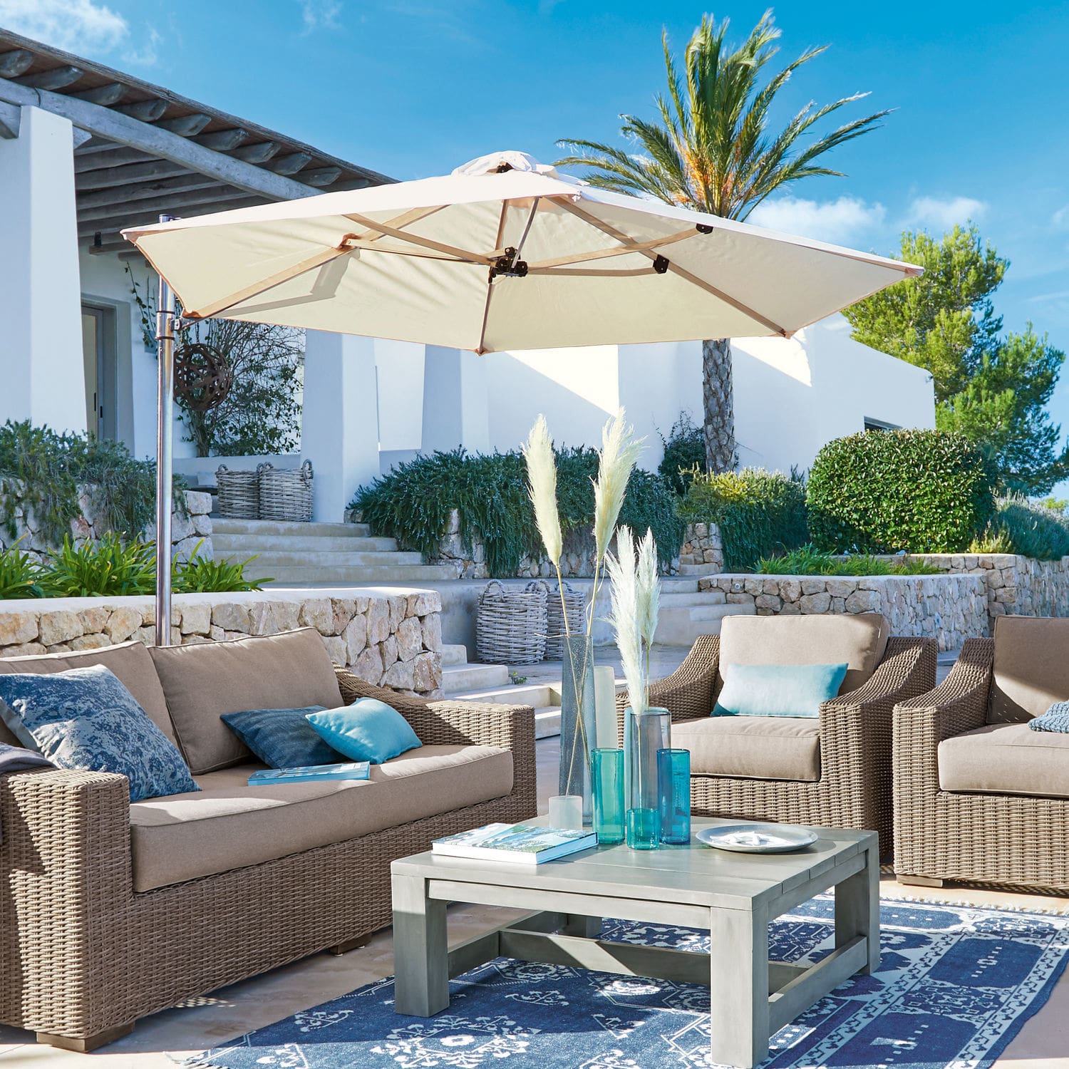Parasol Boudicca Ensemble de mobilier de jardin en rotin synthétique beige avec parasol crème sur terrasse avec tapis bleu