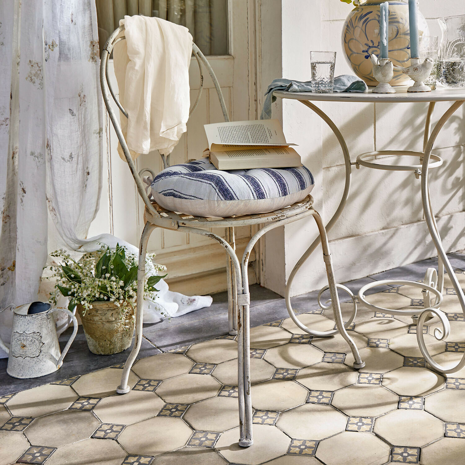 Chaise Aube Chaise en métal vintage avec coussin rayé bleu et blanc, drap blanc sur dossier dans une pièce lumineuse