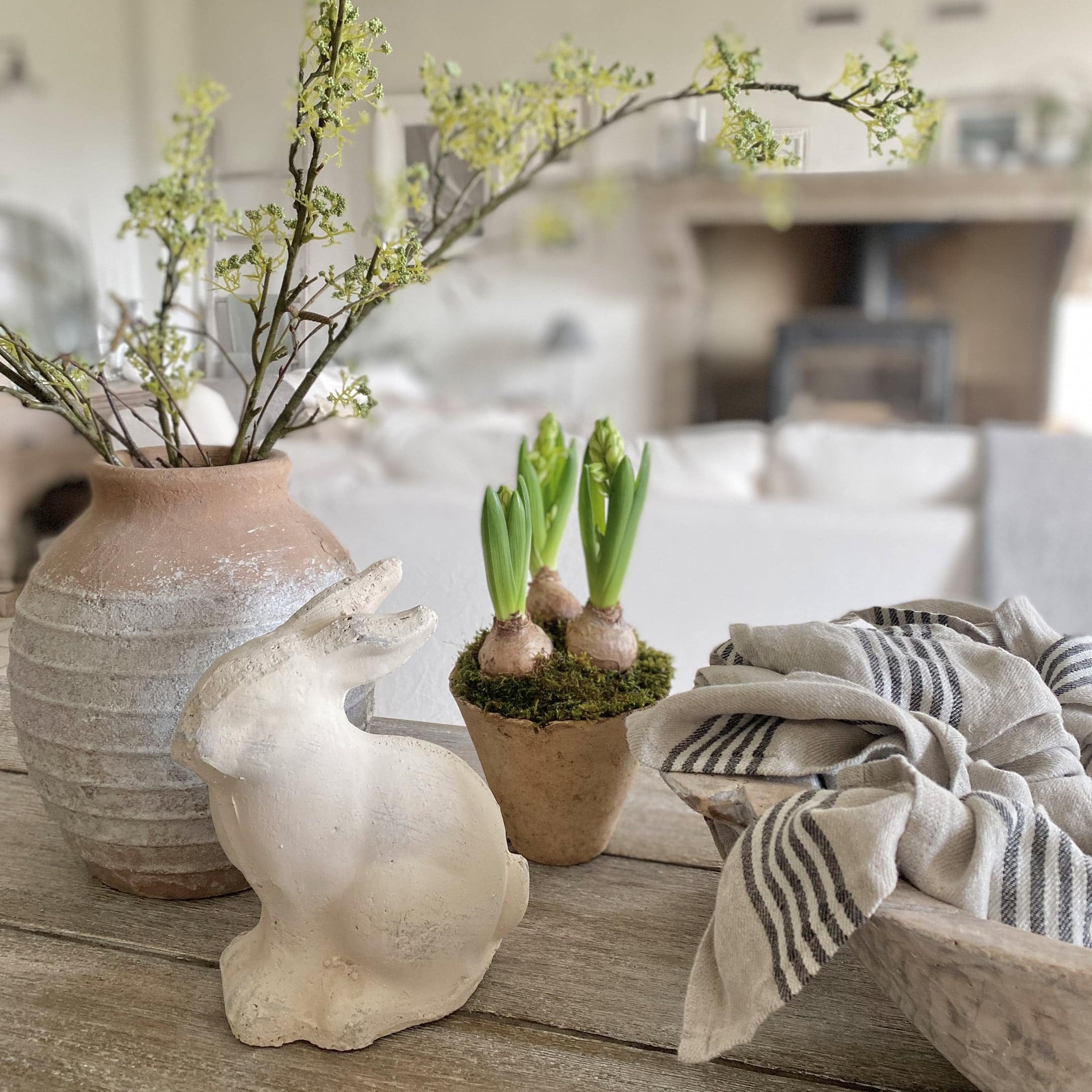 Lapin décoratif blanc en céramique à côté d'un pot avec des pousses vertes et un tissu en lin sur une table en bois