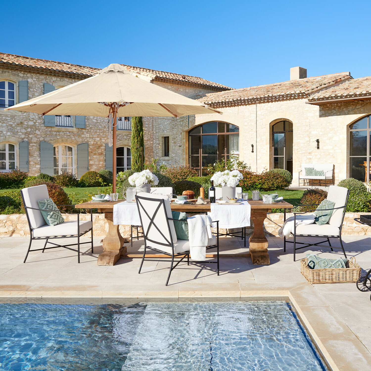 Ensemble de mobilier de jardin avec parasol beige et coussins près de la piscine devant une maison en pierre