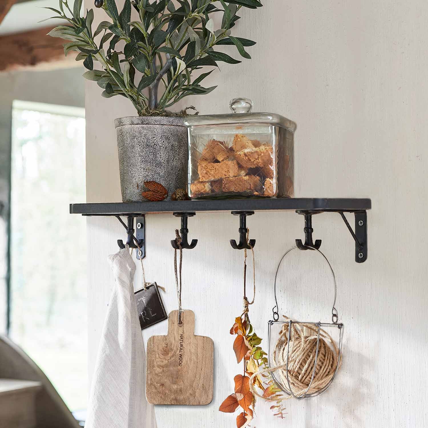 Étagère murale noire en métal avec crochets, plante en pot et boîte en verre remplie de biscuits