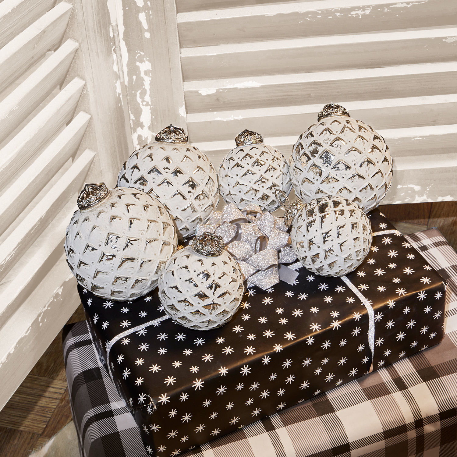 Lot de 6 décorations de Noël Ambria Boules de Noël blanches à motif quadrillé posées sur des cadeaux noirs et blancs dans un décor rustique