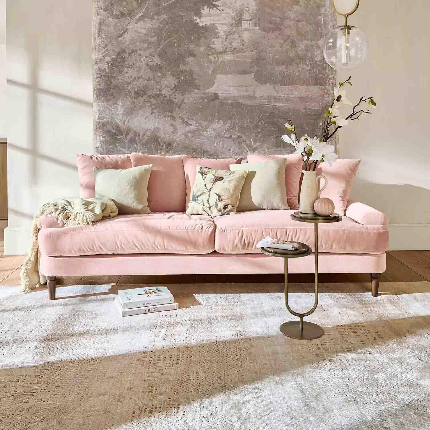 Canapé en velours rose avec coussins et table d'appoint dans un salon lumineux avec décoration murale