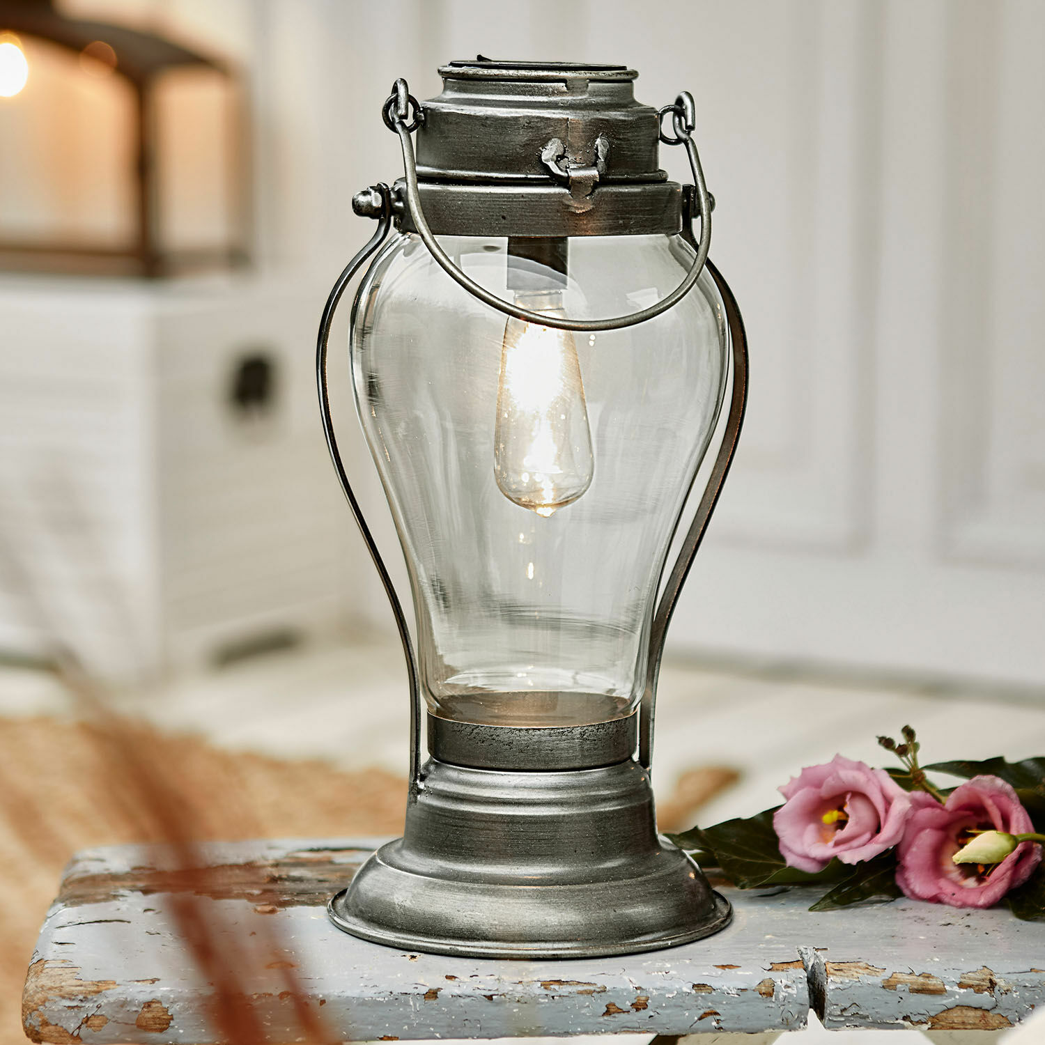 Lanterne solaire Melini Lanterne en métal avec abat-jour en verre transparent et lumière chaude sur une table en bois