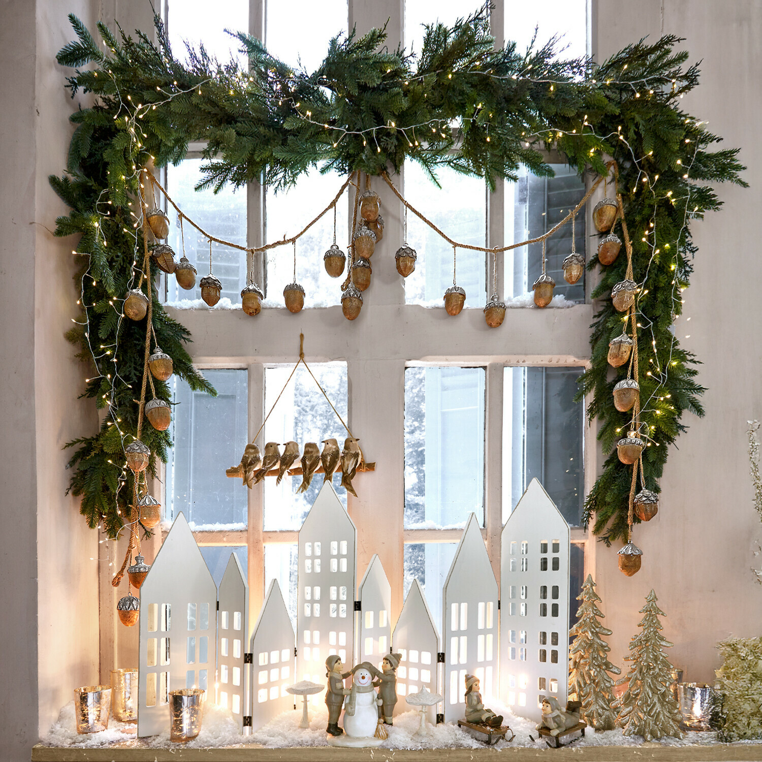 Guirlande Julien Décoration de Noël avec maisons blanches, figurines d'enfants et bonhomme de neige, branches vertes et guirlandes lumineuses