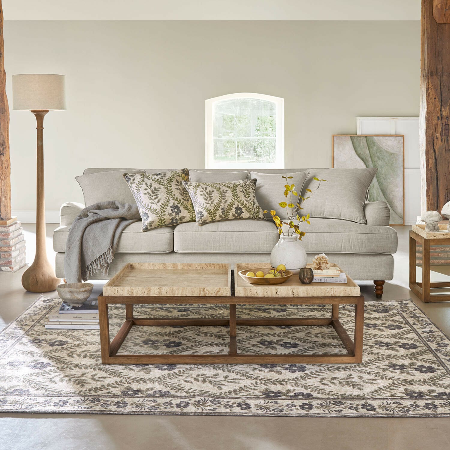 Canapé beige en tissu avec coussins décoratifs et table basse en bois sur tapis à motifs dans un salon lumineux