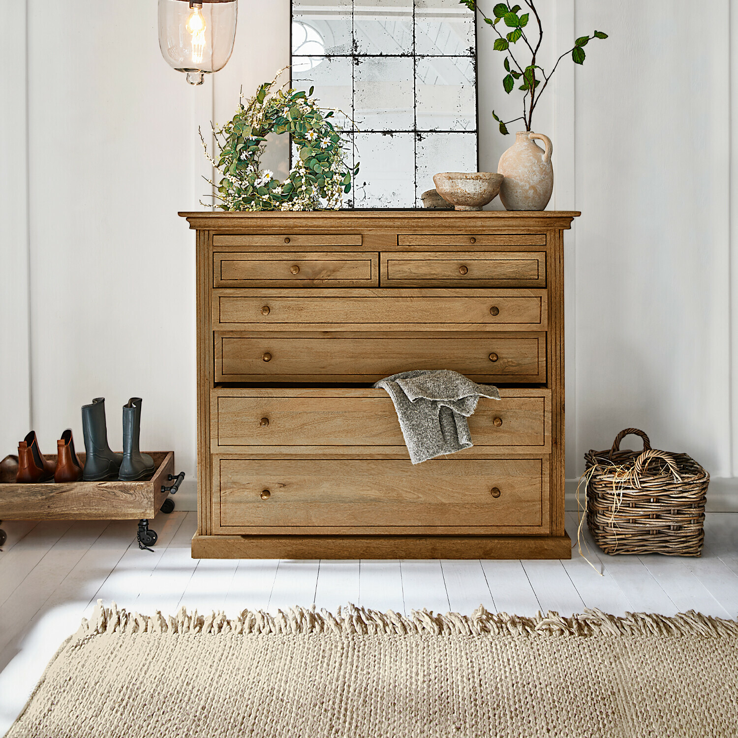 Commode Espoirin Commode en bois naturel avec plusieurs tiroirs, décorations et tapis clair dans un intérieur lumineux