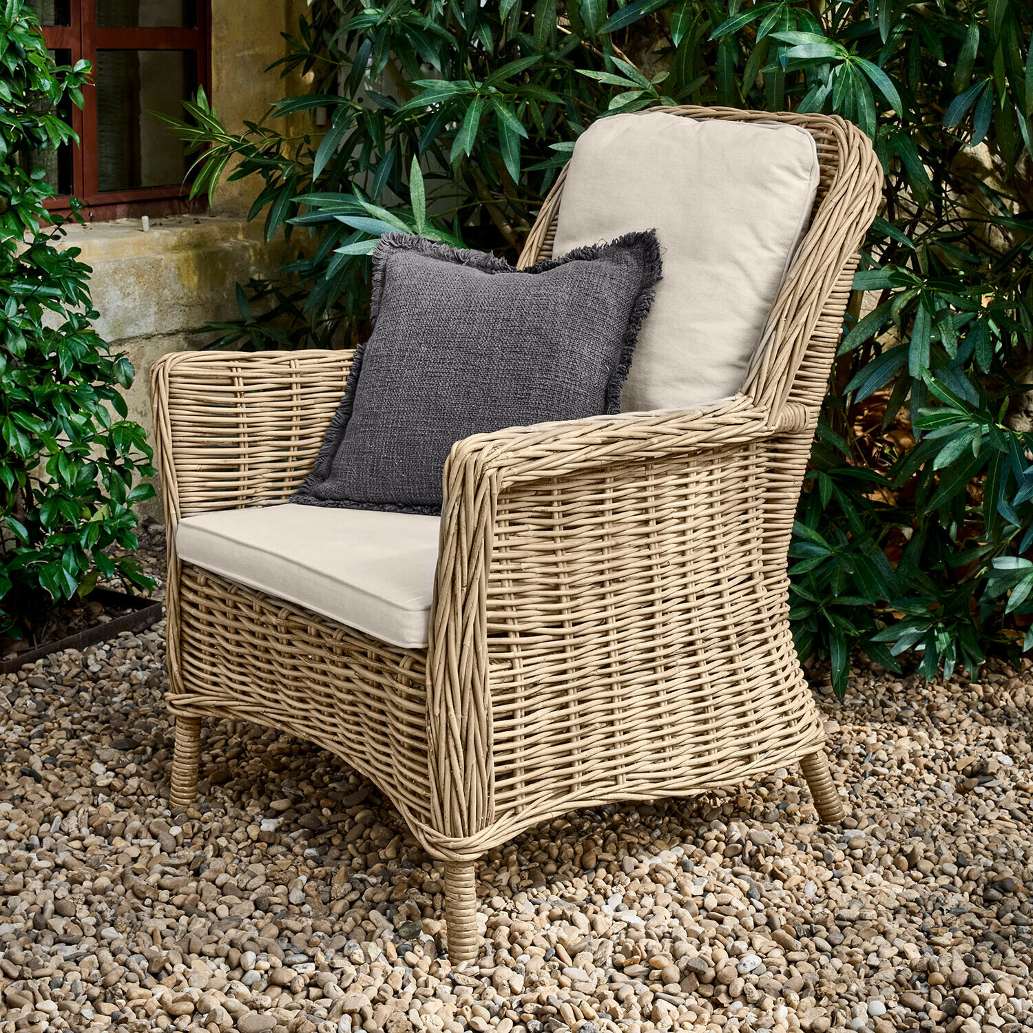 Fauteuil Travenne Fauteuil en rotin avec coussins crème et coussin décoratif gris foncé sur patio en gravier