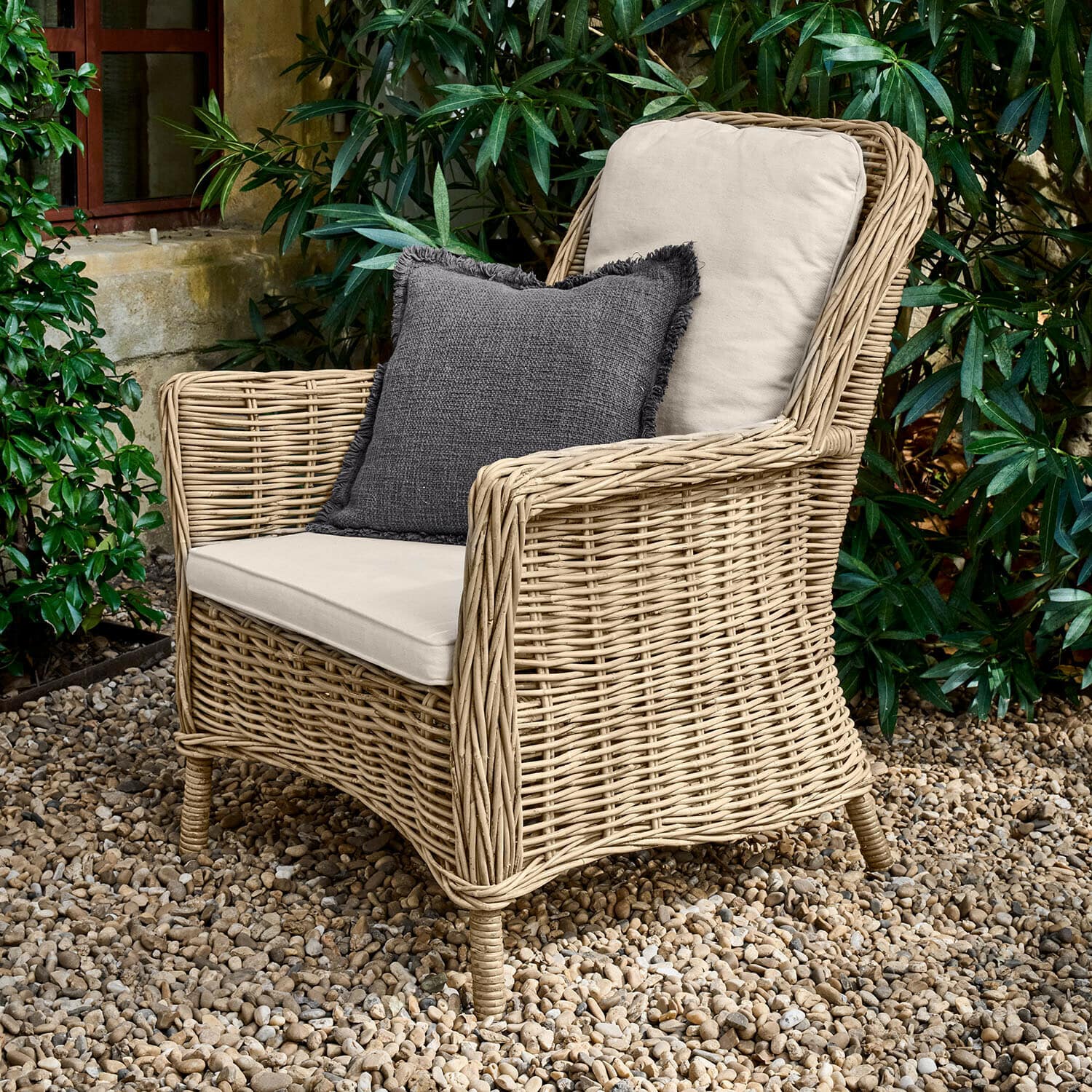 Fauteuil Travenne Fauteuil en rotin avec coussins crème et coussin décoratif gris foncé sur patio en gravier