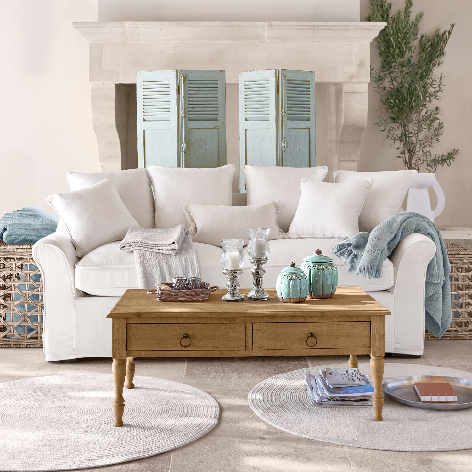 Canapé Long Beach Canapé beige avec coussins et table basse en bois avec décorations dans un salon lumineux avec cheminée