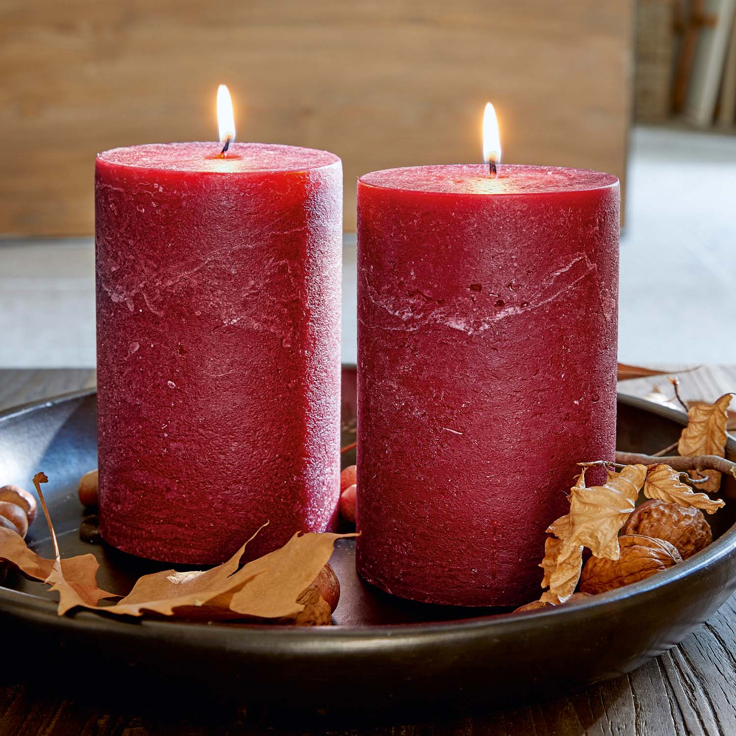 Deux bougies rouges en cire naturelle sur un plateau noir avec feuilles sèches et noix décoratives