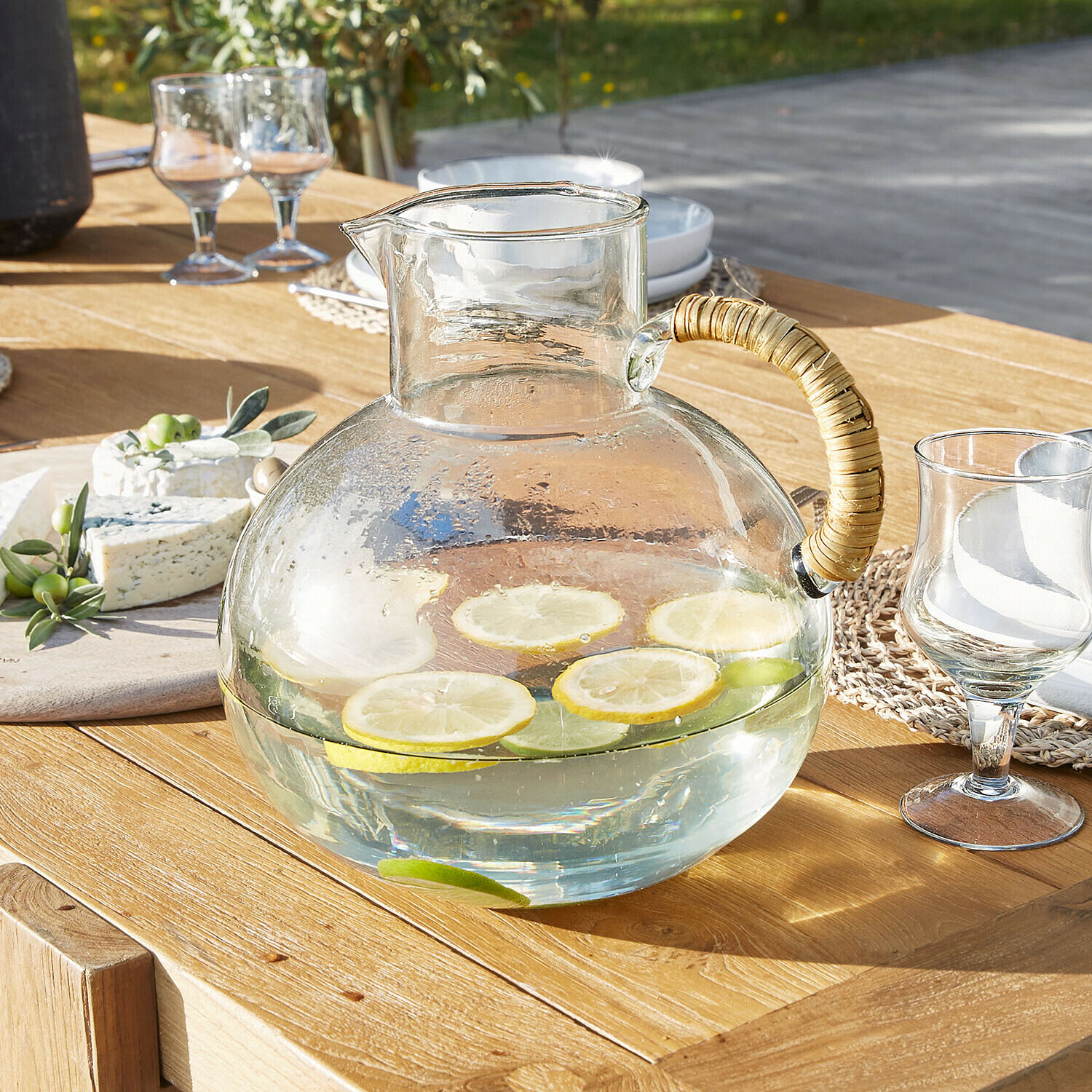 Pichet Stormea Carafe en verre avec anse en rotin sur table en bois, tranches de citron et lime dans l'eau