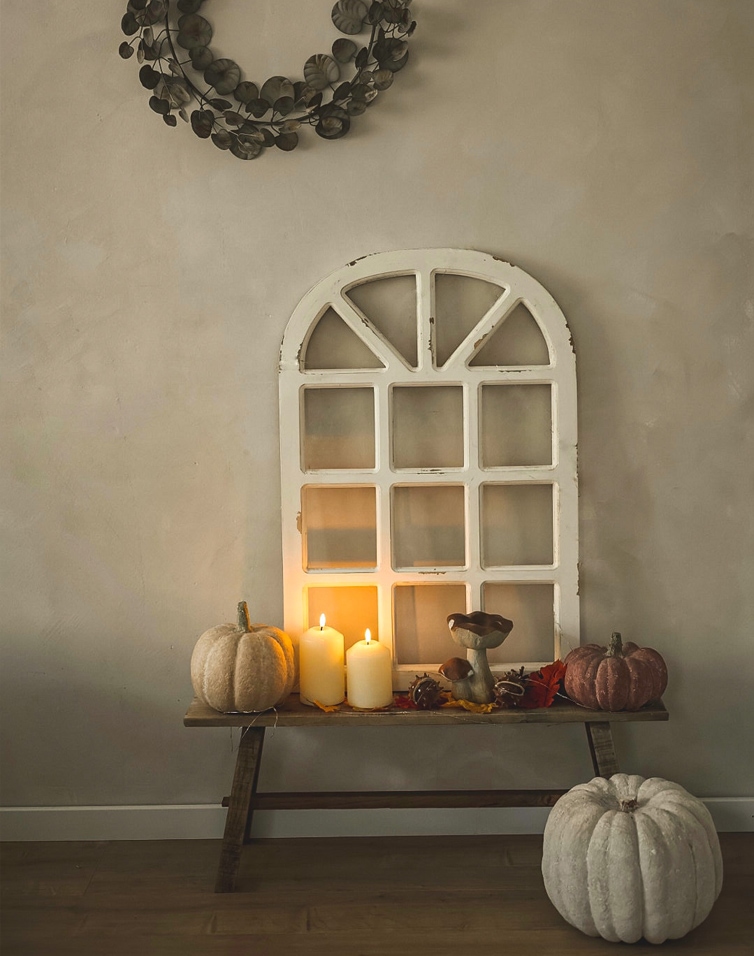 Citrouilles décoratives et bougies sur un banc en bois avec cadre de fenêtre blanc sur mur beige