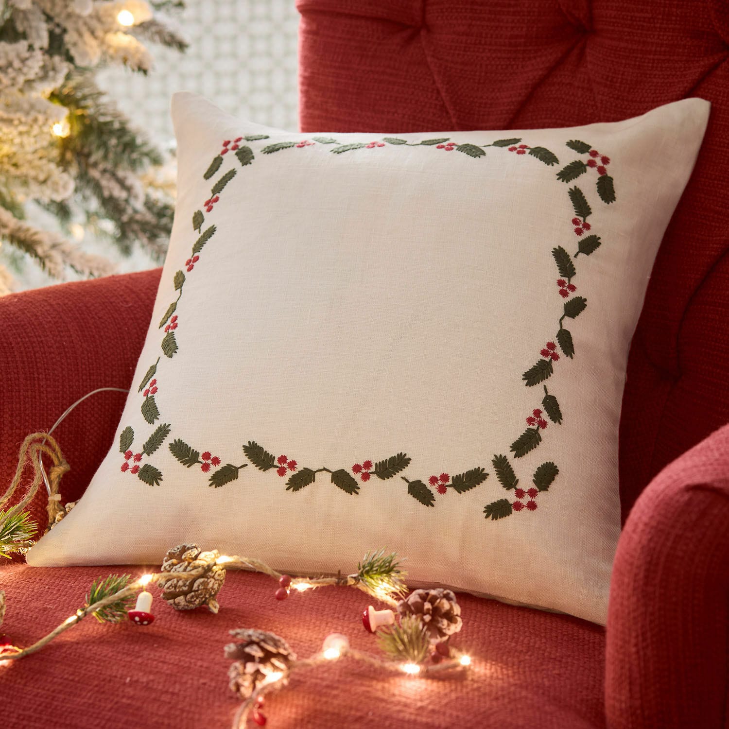Housse de coussin Lenius Coussin en lin blanc avec feuilles vertes et baies rouges sur fauteuil rouge, décoration de Noël