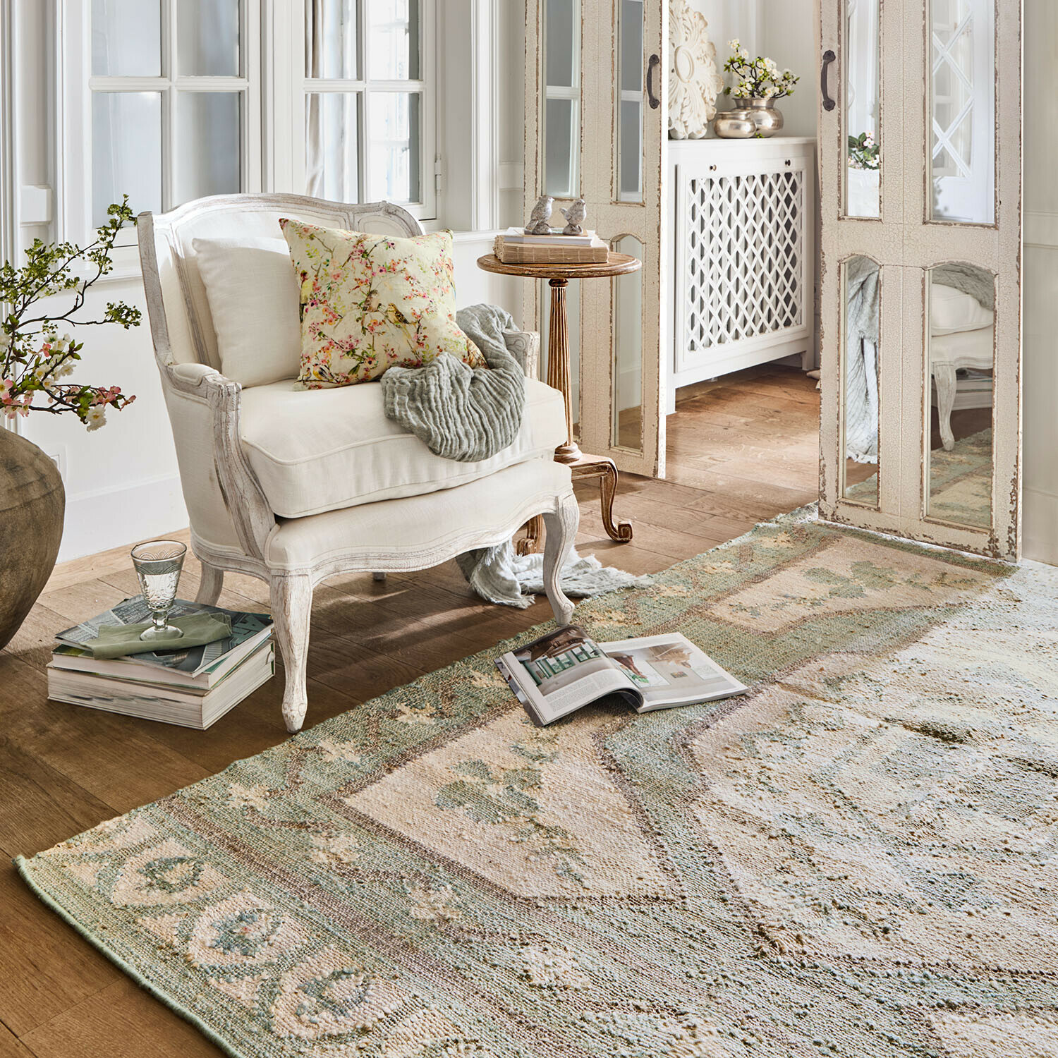 Tapis Raneema Fauteuil blanc en bois avec coussin floral dans un salon lumineux avec tapis vintage aux tons doux