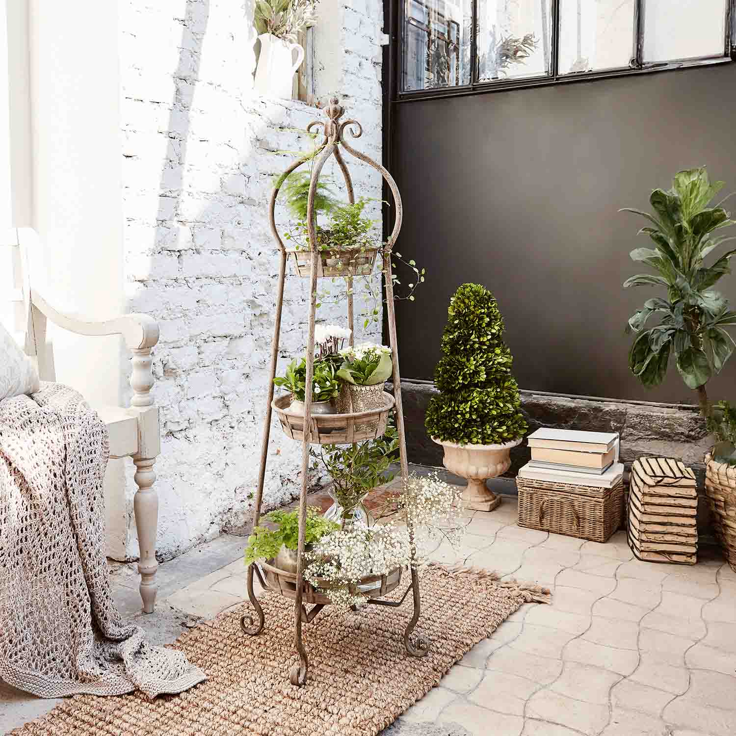 Jardinière sur pied en métal à trois niveaux avec plantes vertes dans un intérieur lumineux à mur en briques blanches