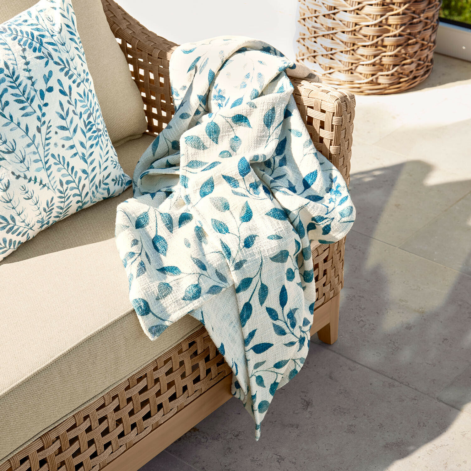 Plaid Ocevara Canapé beige en osier avec coussin et plaid crème à motifs de feuilles bleues pour terrasse