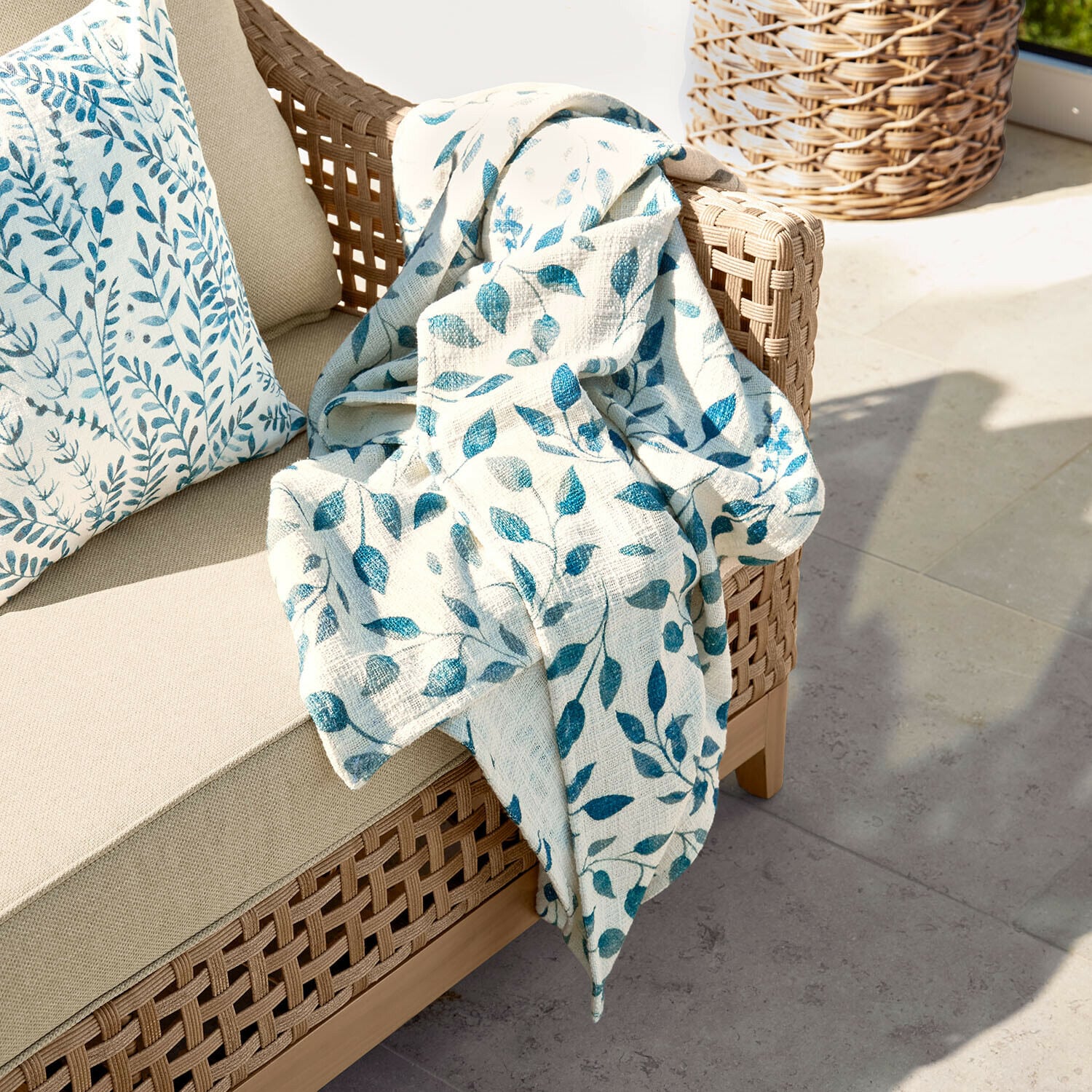 Plaid Ocevara Canapé beige en osier avec coussin et plaid crème à motifs de feuilles bleues pour terrasse