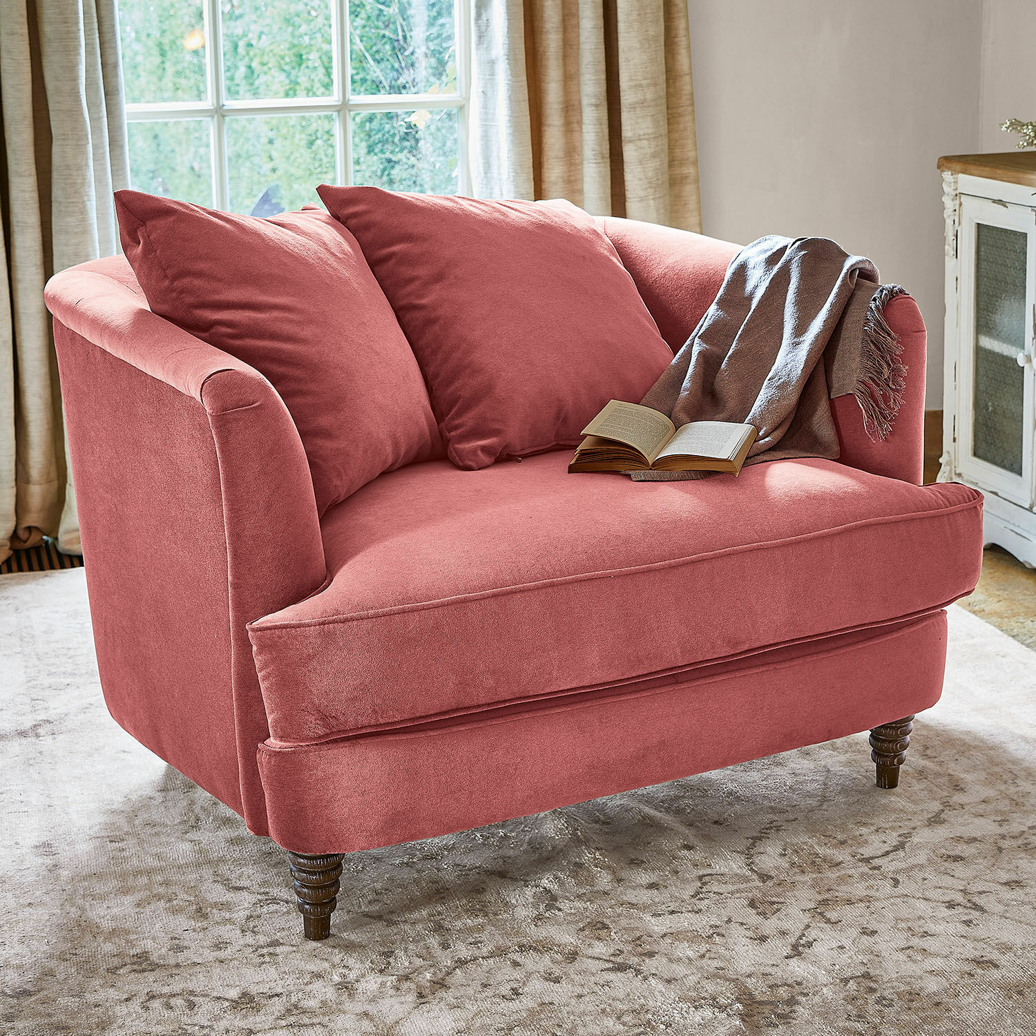 Fauteuil Etueffont Canapé rose en tissu doux avec coussins et plaid gris sur tapis clair dans un salon lumineux