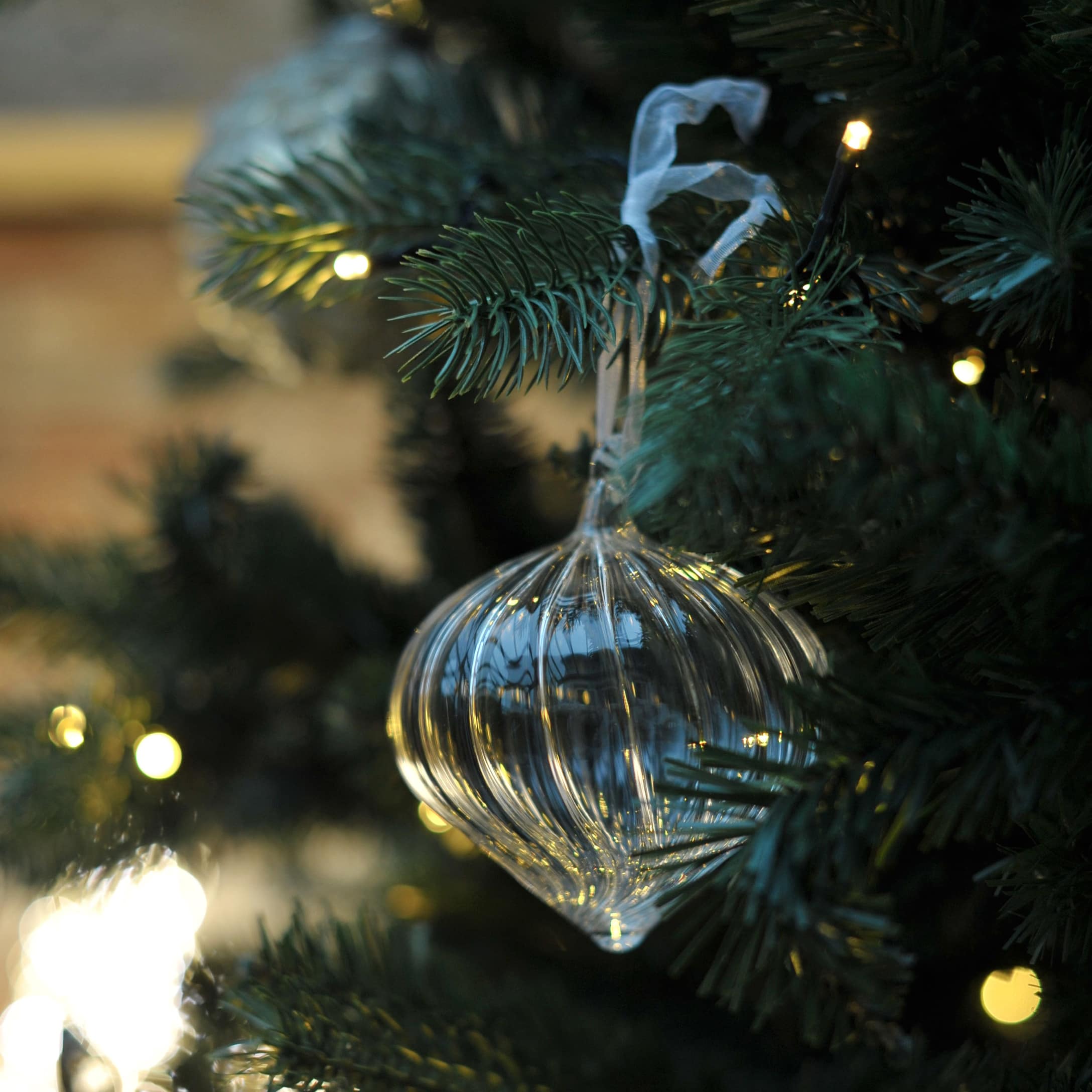 Décoration de sapin en verre transparent en forme d'oignon suspendue à une branche verte avec lumières LED