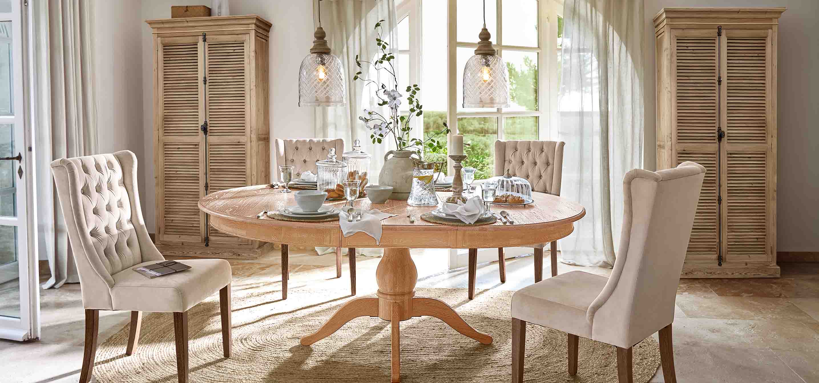 Salle à manger avec table ronde en bois clair et chaises rembourrées beige dans un style vintage