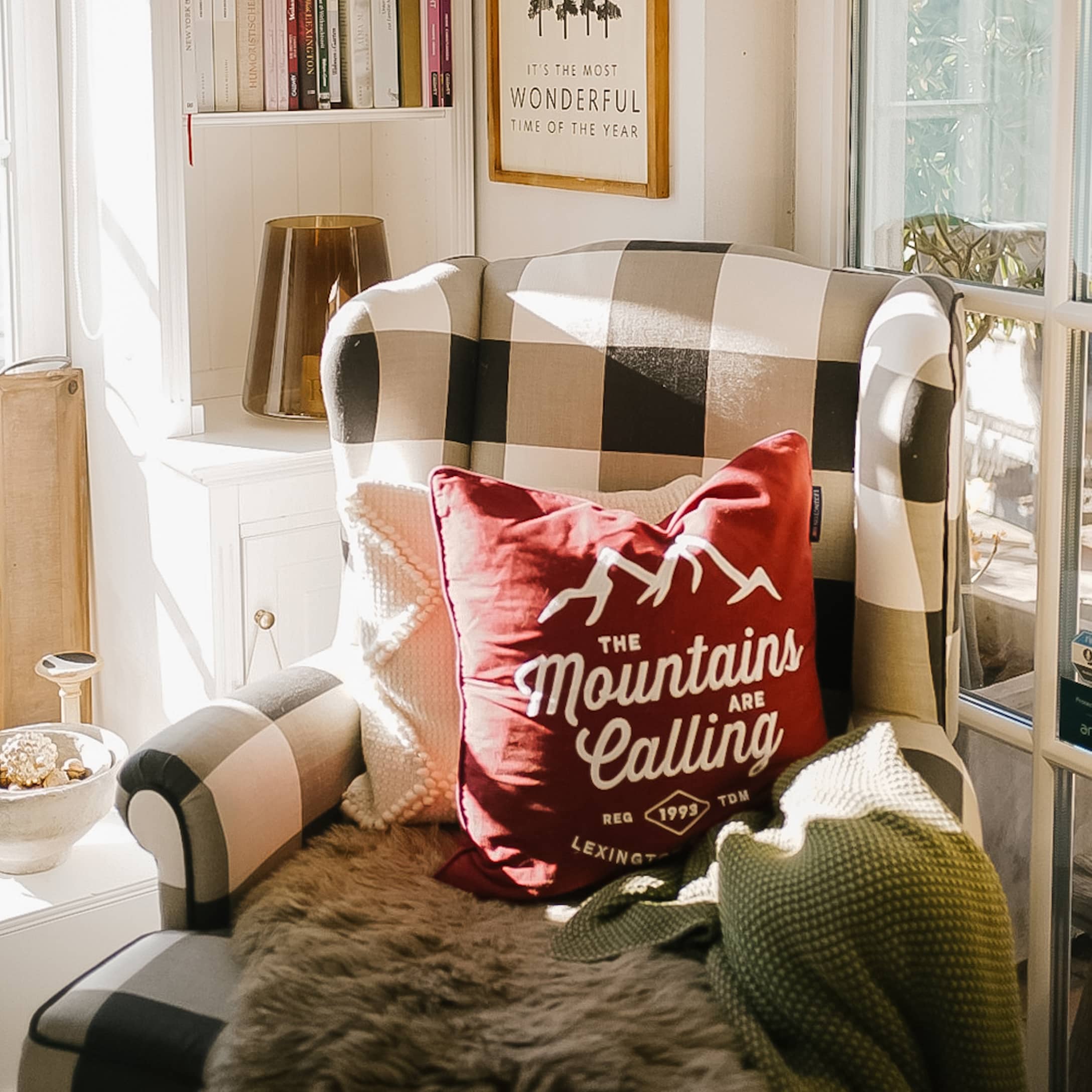 Fauteuil à carreaux avec coussin rouge Mountains et couverture verte dans une pièce lumineuse