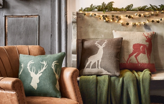 Coussins décoratifs avec motif de cerf en couleurs naturelles sur fauteuil en cuir et banc avec couverture verte