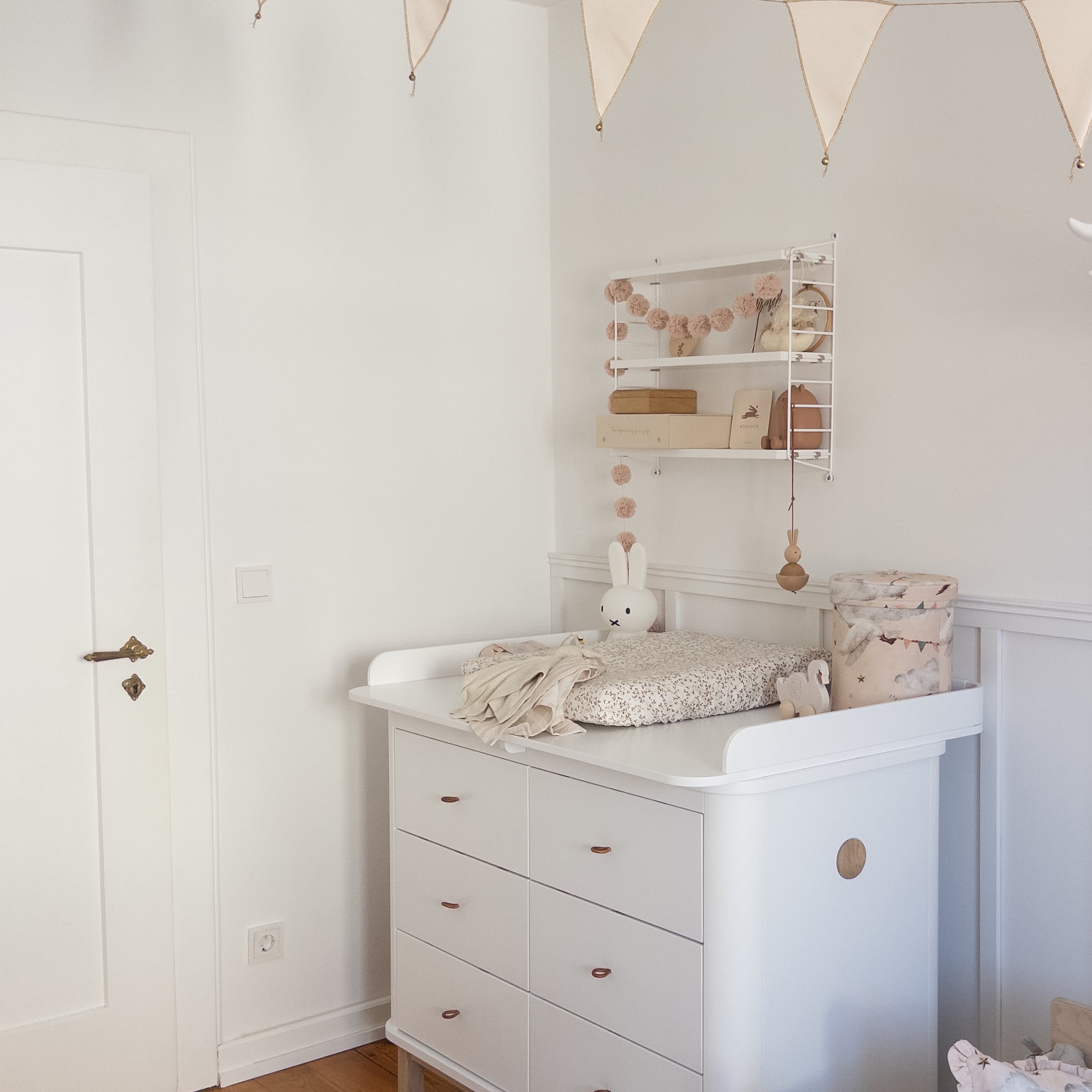 Commode blanche avec table à langer et décorations enfantines pastel dans une chambre d'enfant lumineuse