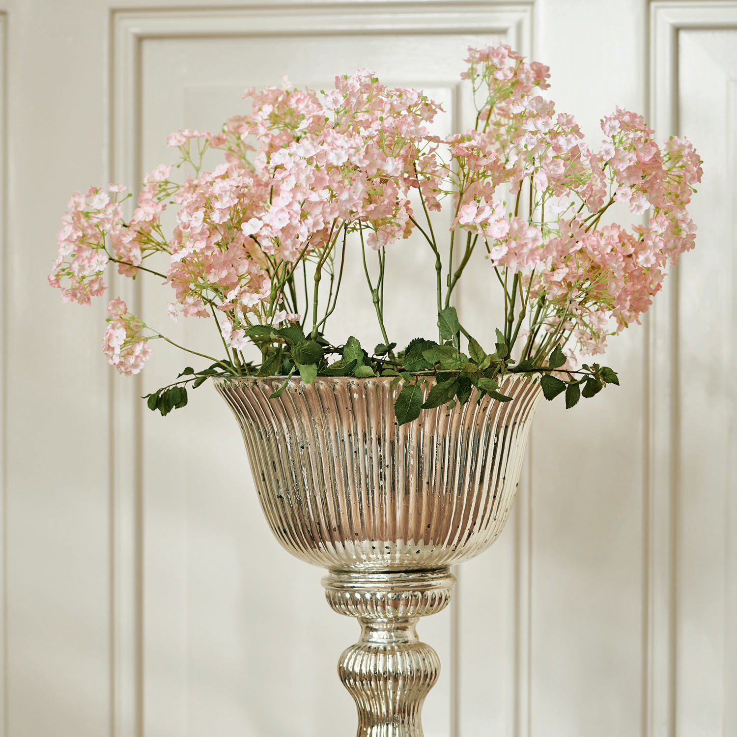 Lot de 4 décorations florales Calanthe Vase en métal argenté avec fleurs roses décoratives devant un mur clair