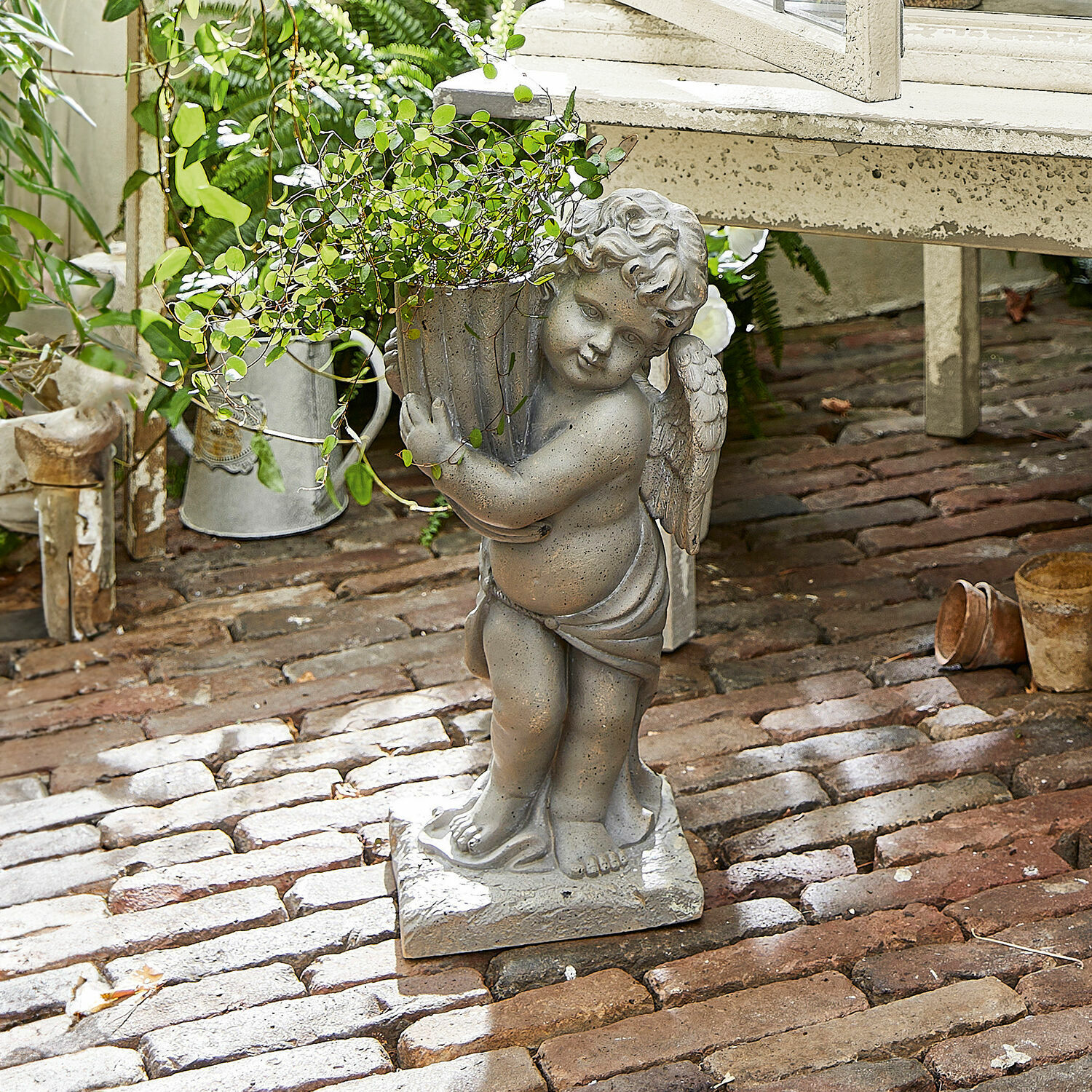 Cache-pot Pirie Statue d'ange en pierre grise tenant un pot avec plante verte sur un sol en briques
