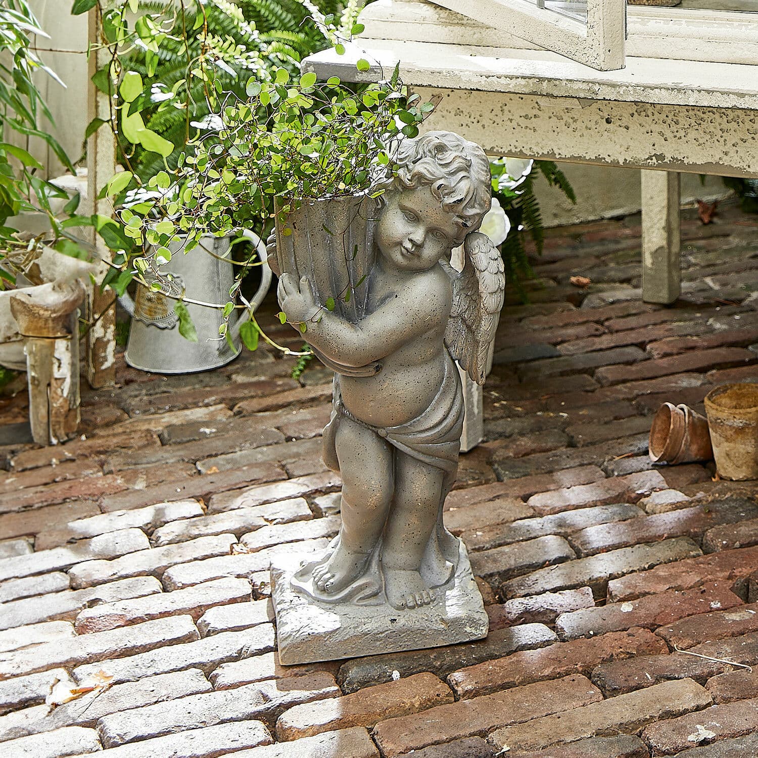 Cache-pot Pirie Statue d'ange en pierre grise tenant un pot avec plante verte sur un sol en briques