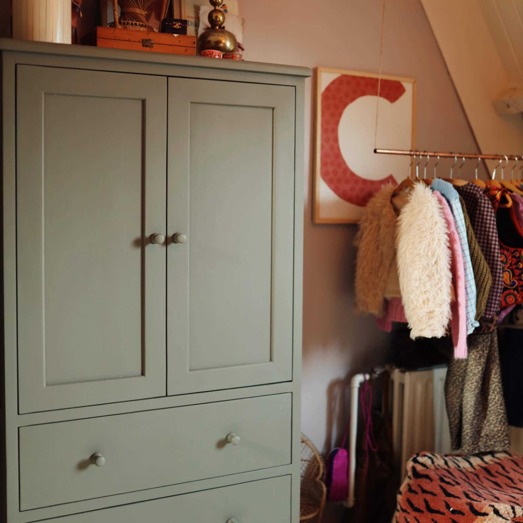 Armoire en bois grise avec deux tiroirs dans une pièce chaleureuse avec vêtements suspendus