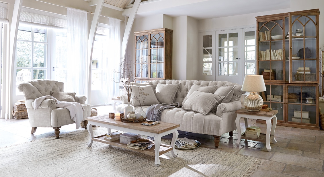 Salon chaleureux style campagne avec canapé beige en tissu, fauteuil assorti, meubles en bois et tapis clair