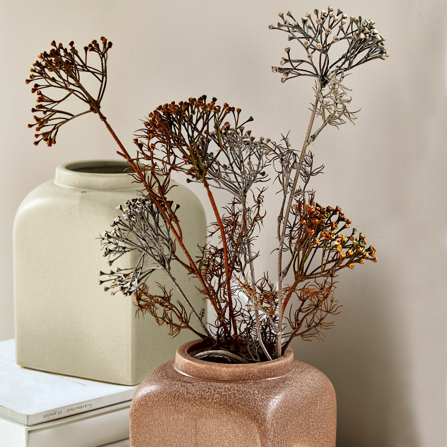 Lot de 4 fleurs décoratives Jennings Vase en céramique marron avec fleurs séchées devant une décoration beige et des livres