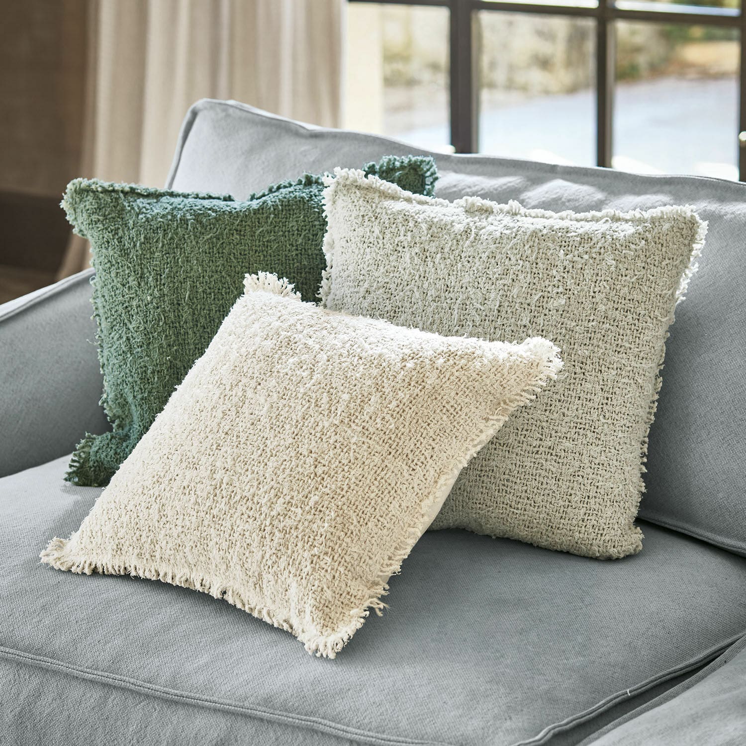 Lot de 3 housses de coussins Juliana Trois coussins décoratifs en tissu beige et vert posés sur un canapé gris clair