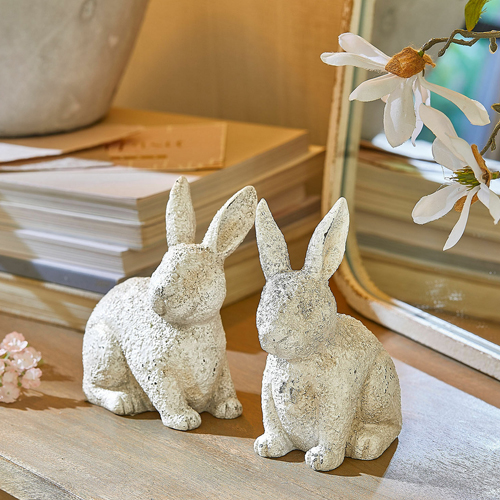 Deux figurines de lapins blanches en matériau texturé sur une table en bois, décoration printanière