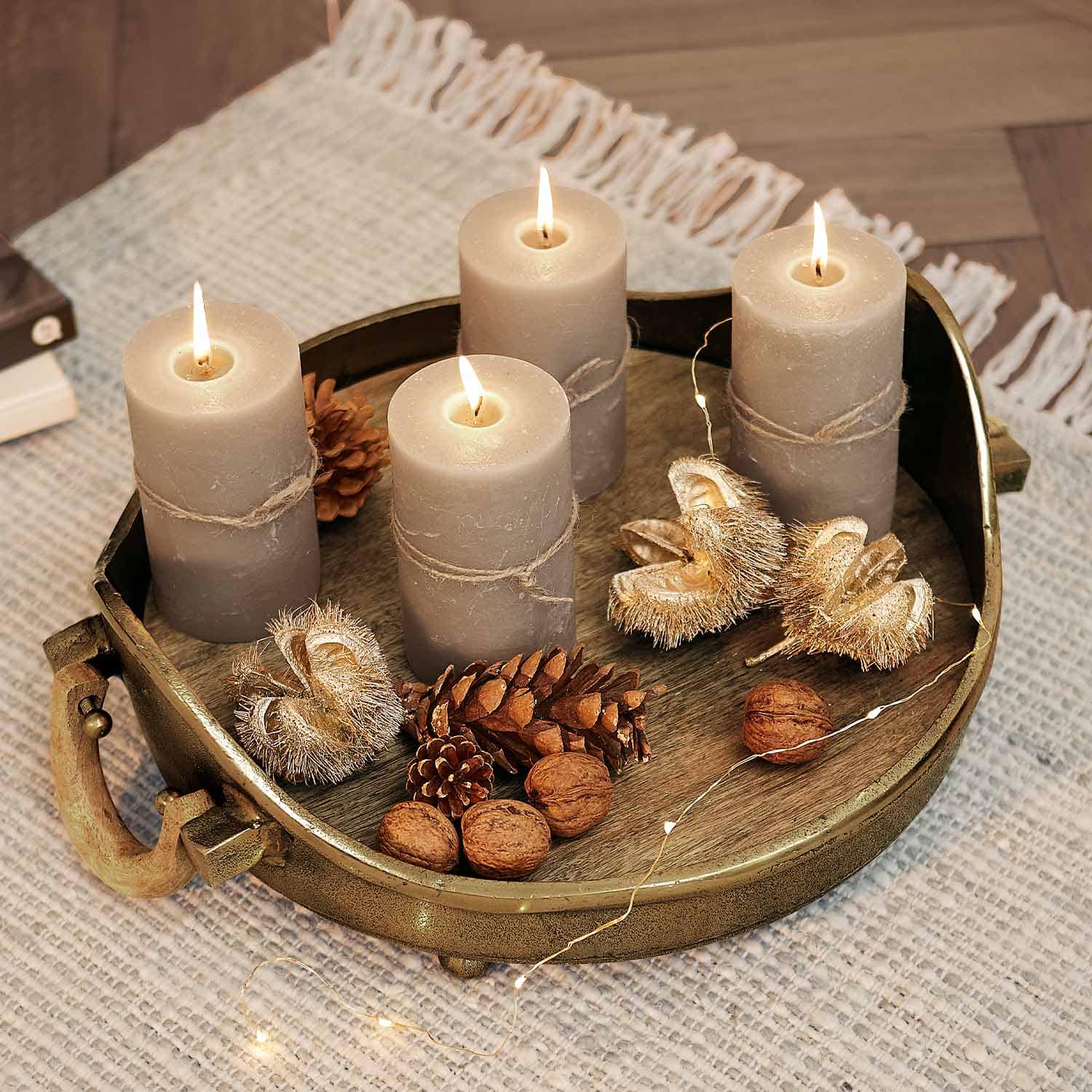 Quatre bougies grises avec ficelle de jute sur un plateau en métal avec décorations de pommes de pin et noix