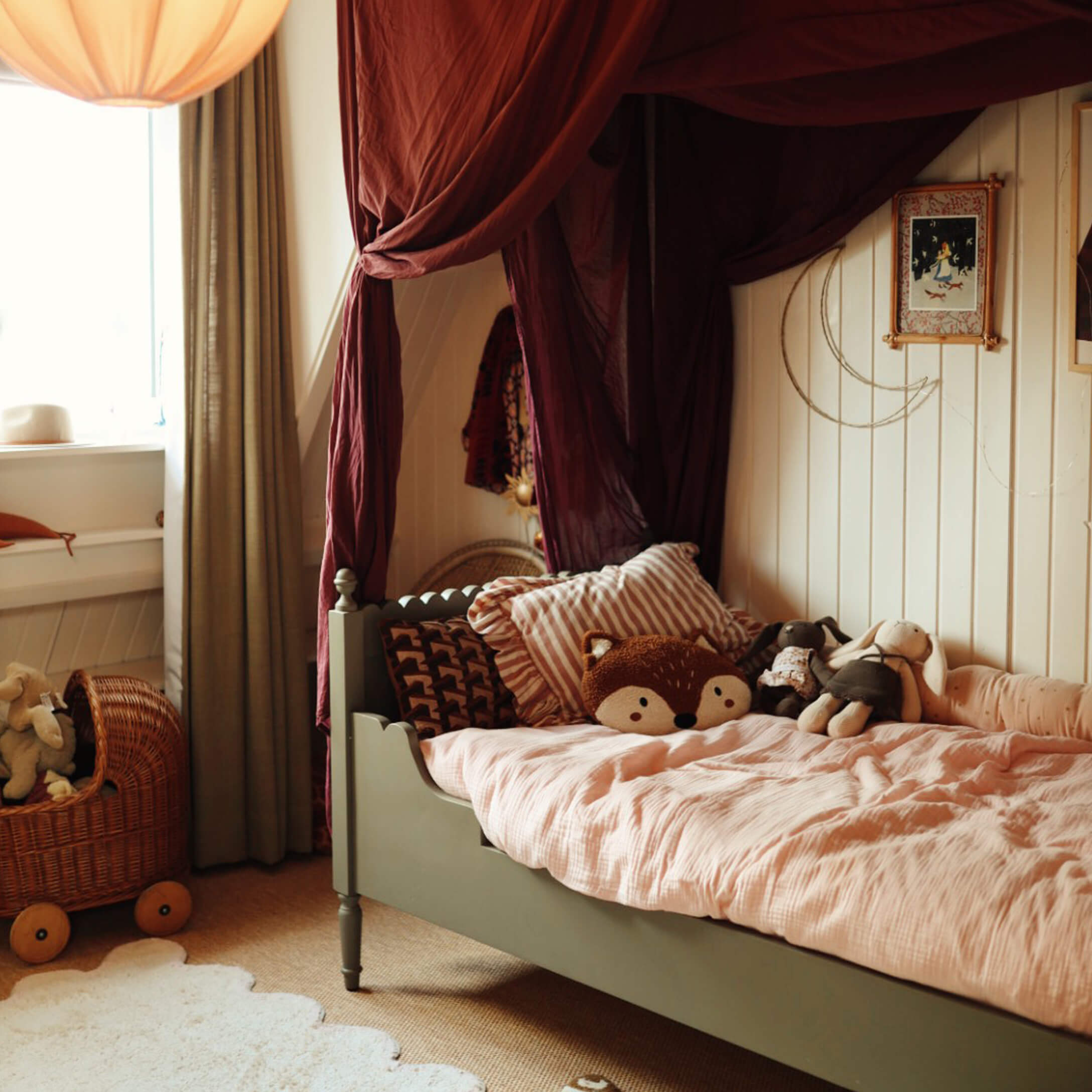Lit enfant vert avec couette rose et peluches dans une chambre chaleureuse avec rideaux bordeaux