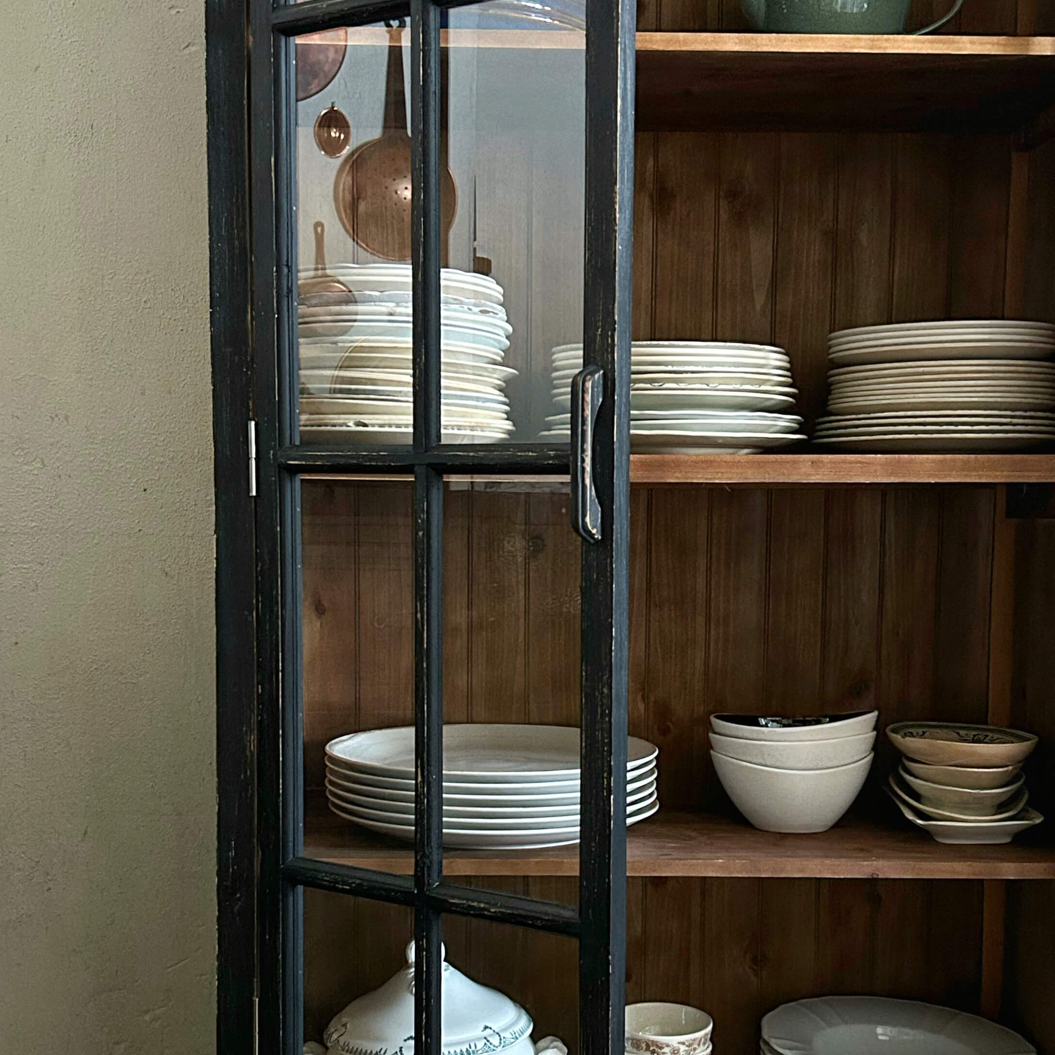 Porte noire en bois avec vitre d'armoire, à l'intérieur assiettes blanches et bols sur étagères en bois