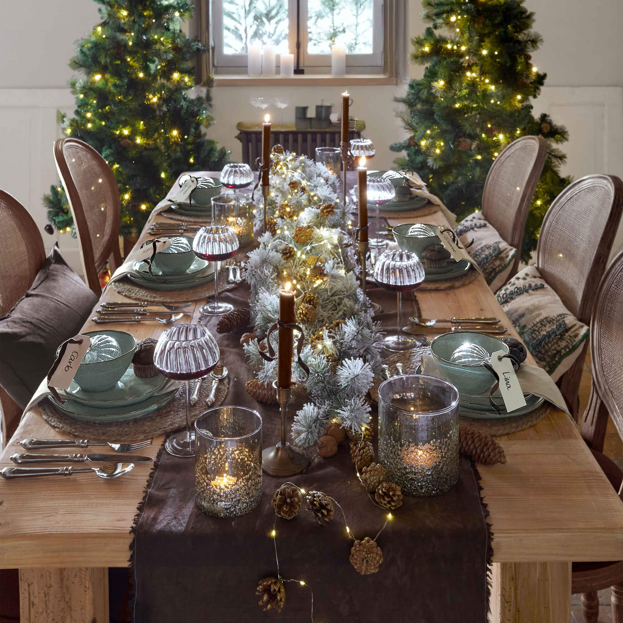 Table en bois décorée pour Noël avec vaisselle verte, bougies et guirlandes lumineuses LED