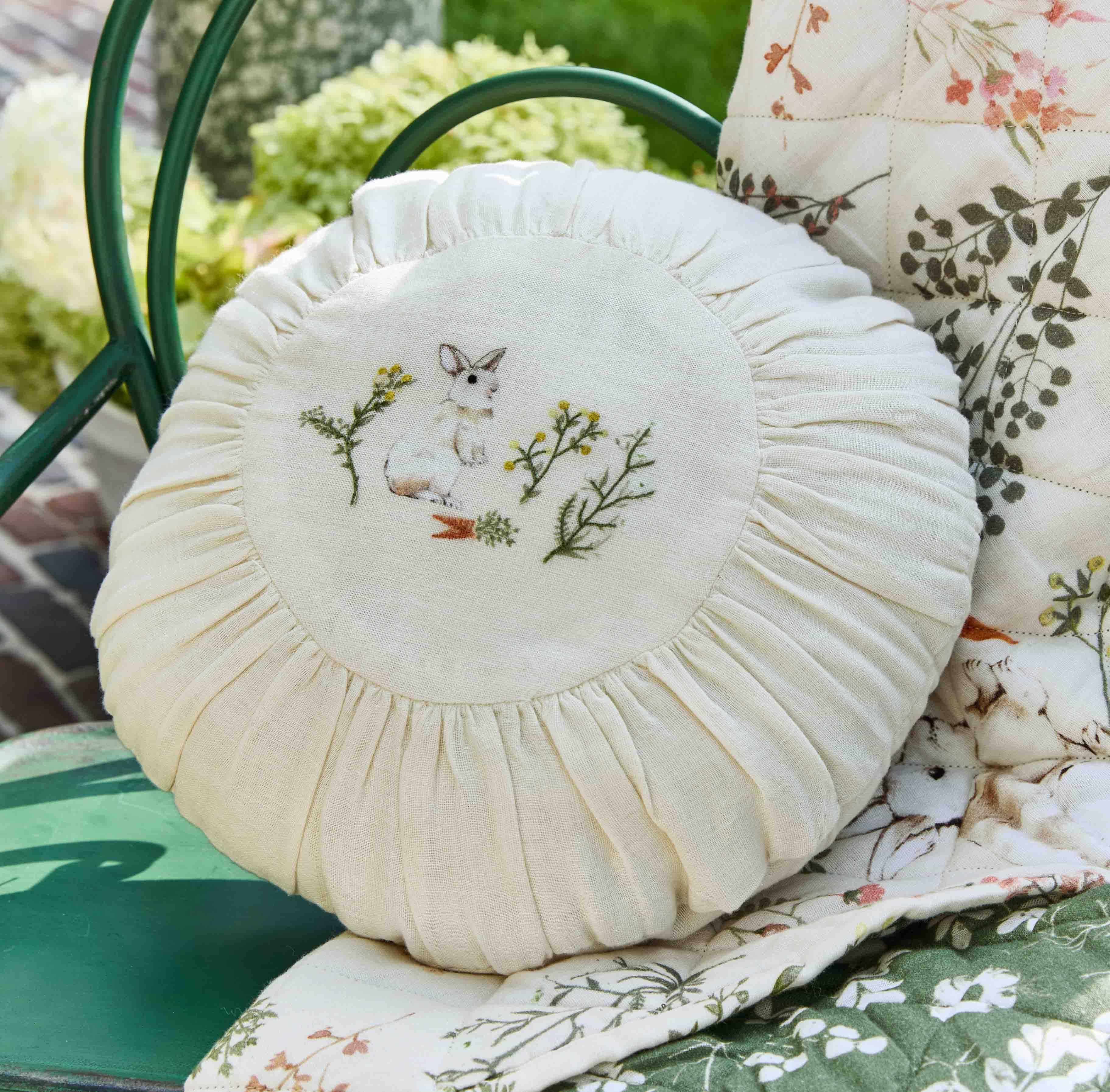 Coussin rond crème avec broderie de lapin blanc et plantes vertes sur chaise de jardin