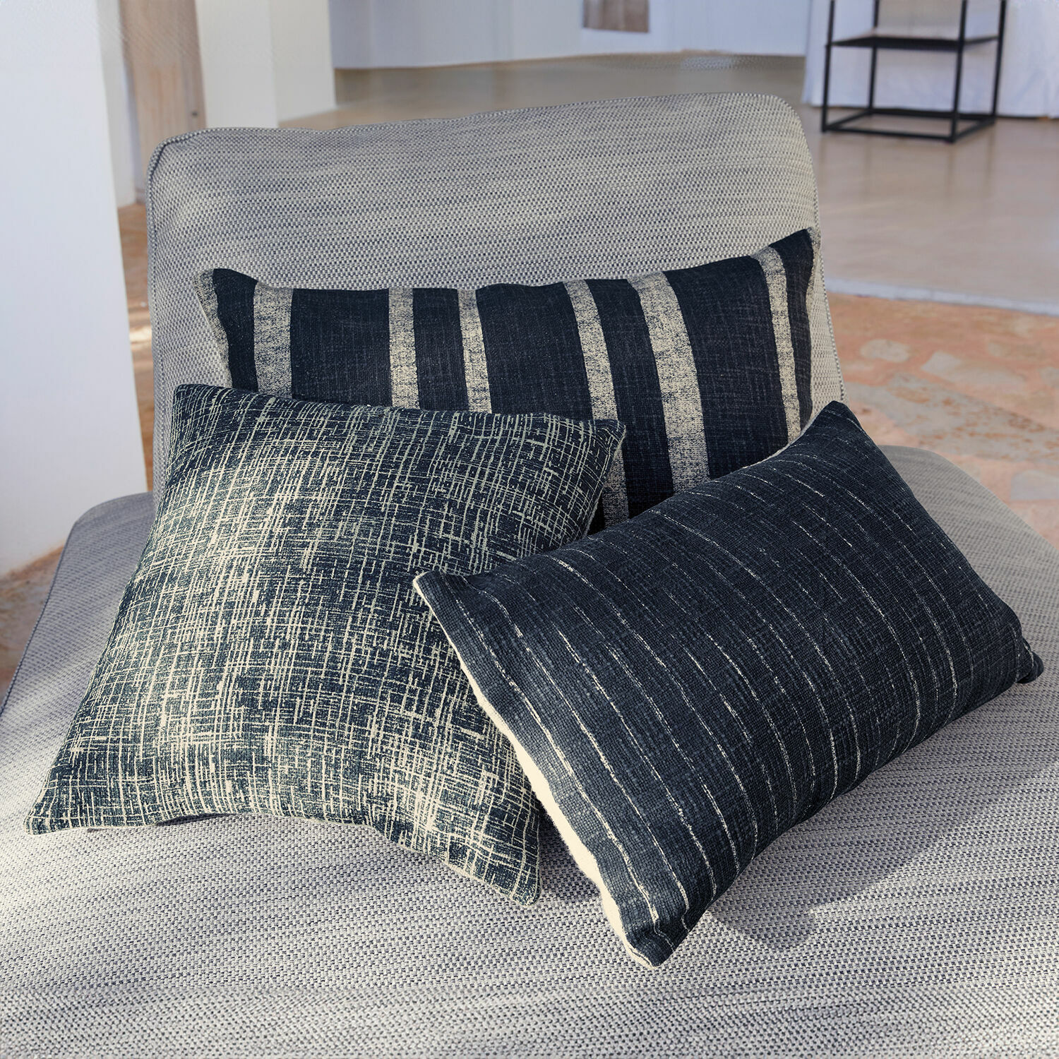 Lot de 3 housses de coussins Andulo Trois coussins décoratifs noirs et blancs avec motifs sur un fauteuil gris clair dans un salon
