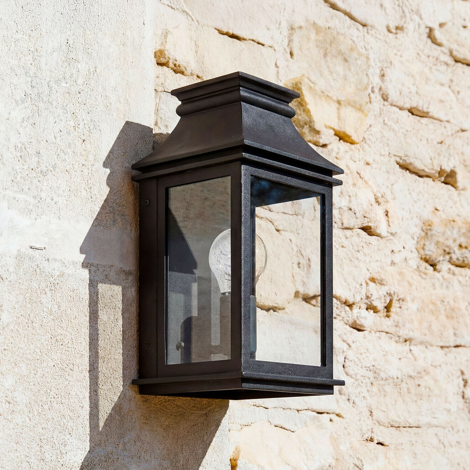 Applique murale noire en métal avec verre transparent sur mur en pierre claire, éclairage extérieur classique