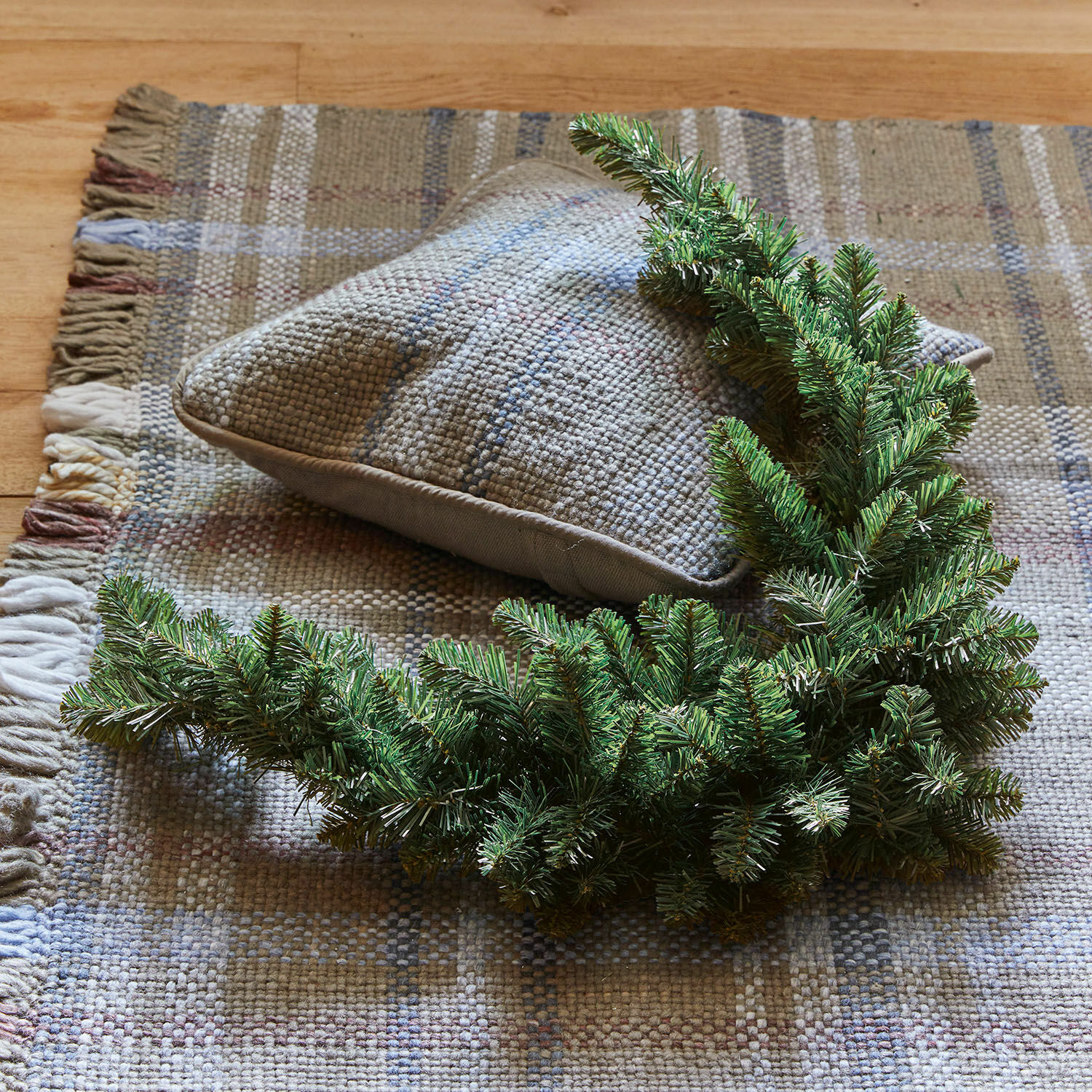 Guirlande Melis Couronne décorative verte en feuillage sur un tapis beige tissé avec un coussin