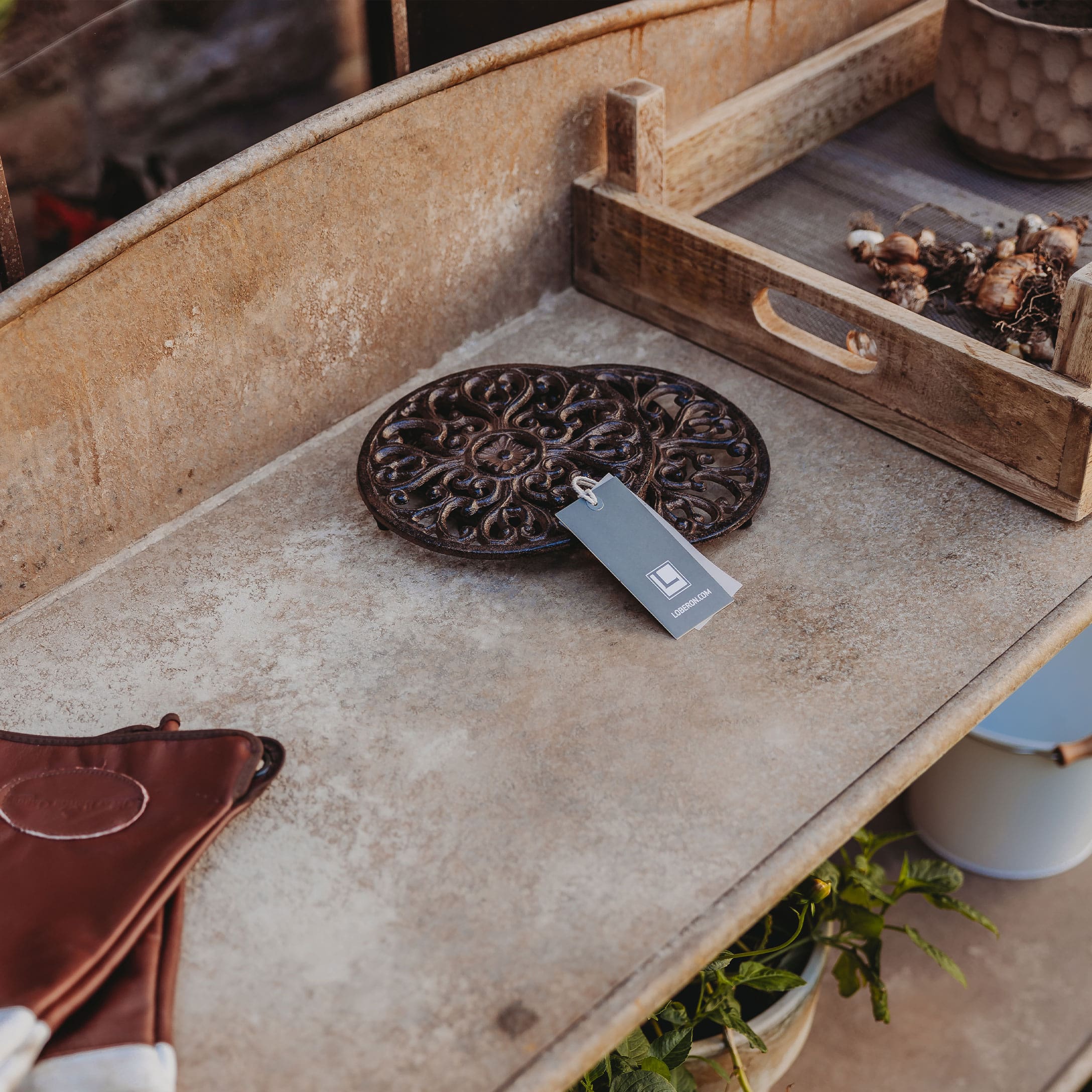Dessous de plat rond en métal foncé avec motif décoratif sur table rustique de jardin