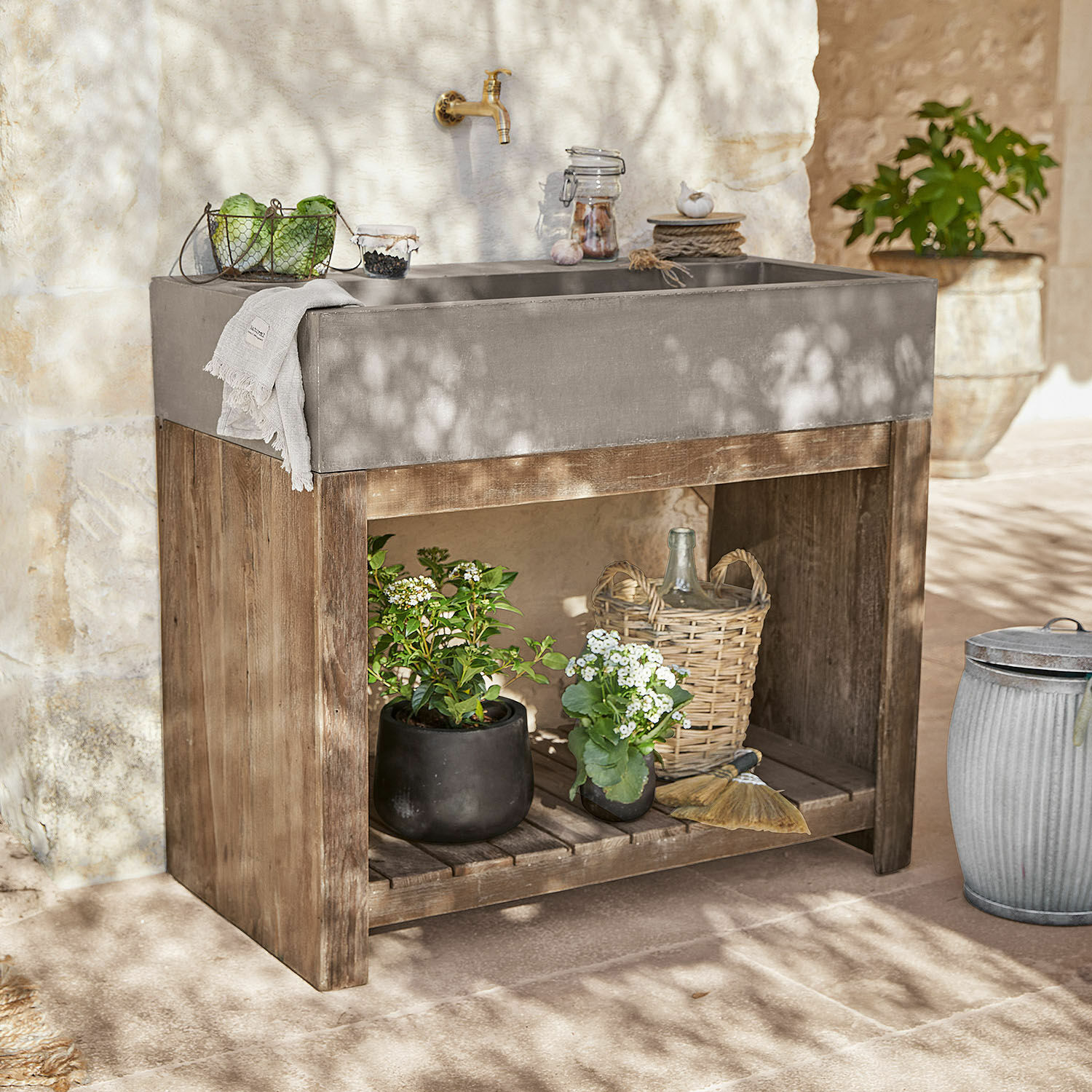 Meuble avec vasque Baines Évier en béton gris sur support en bois avec plantes et décorations dans un jardin ensoleillé